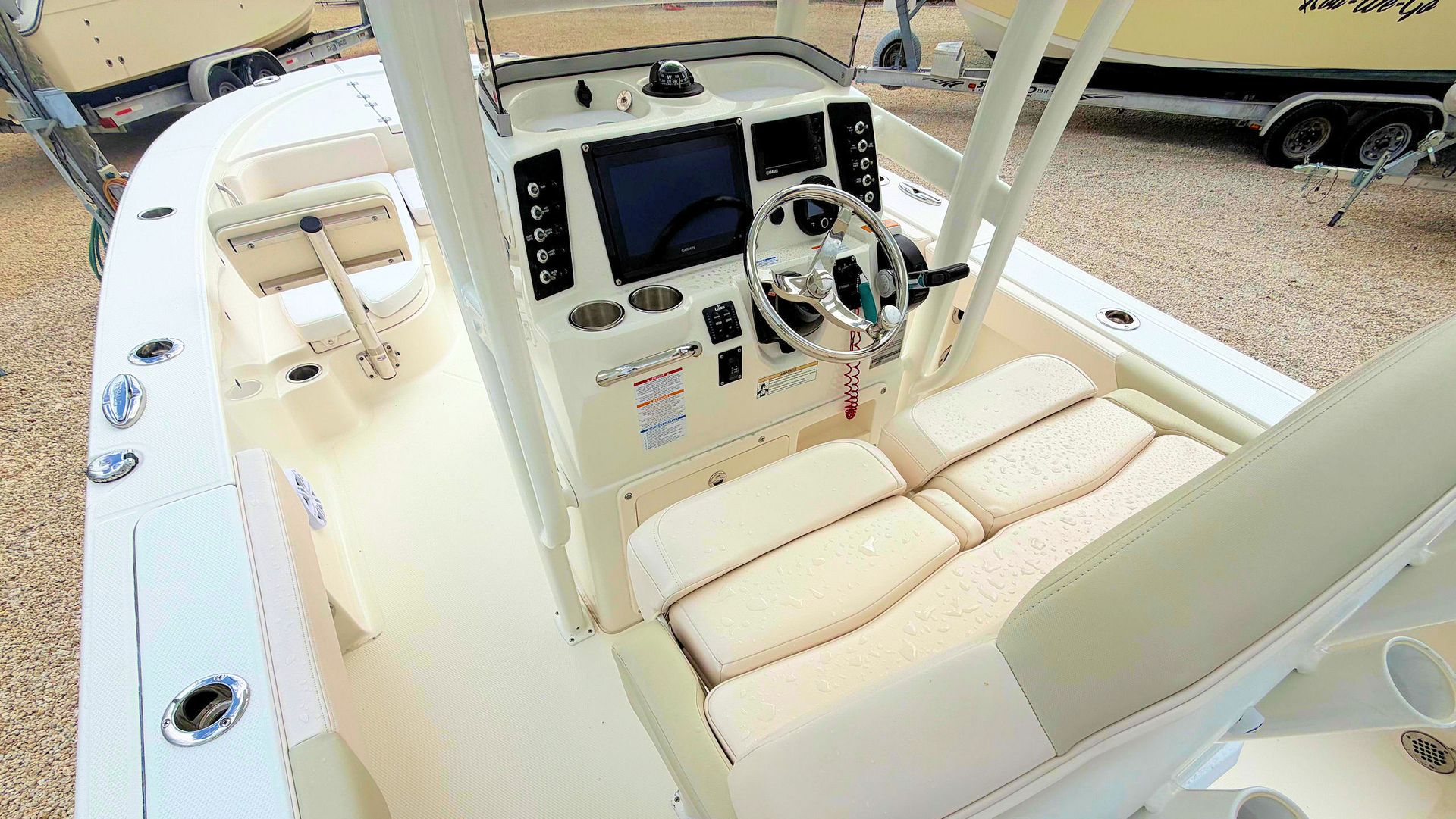 Boat helm with cream seats, steering console, and controls on a beige deck.