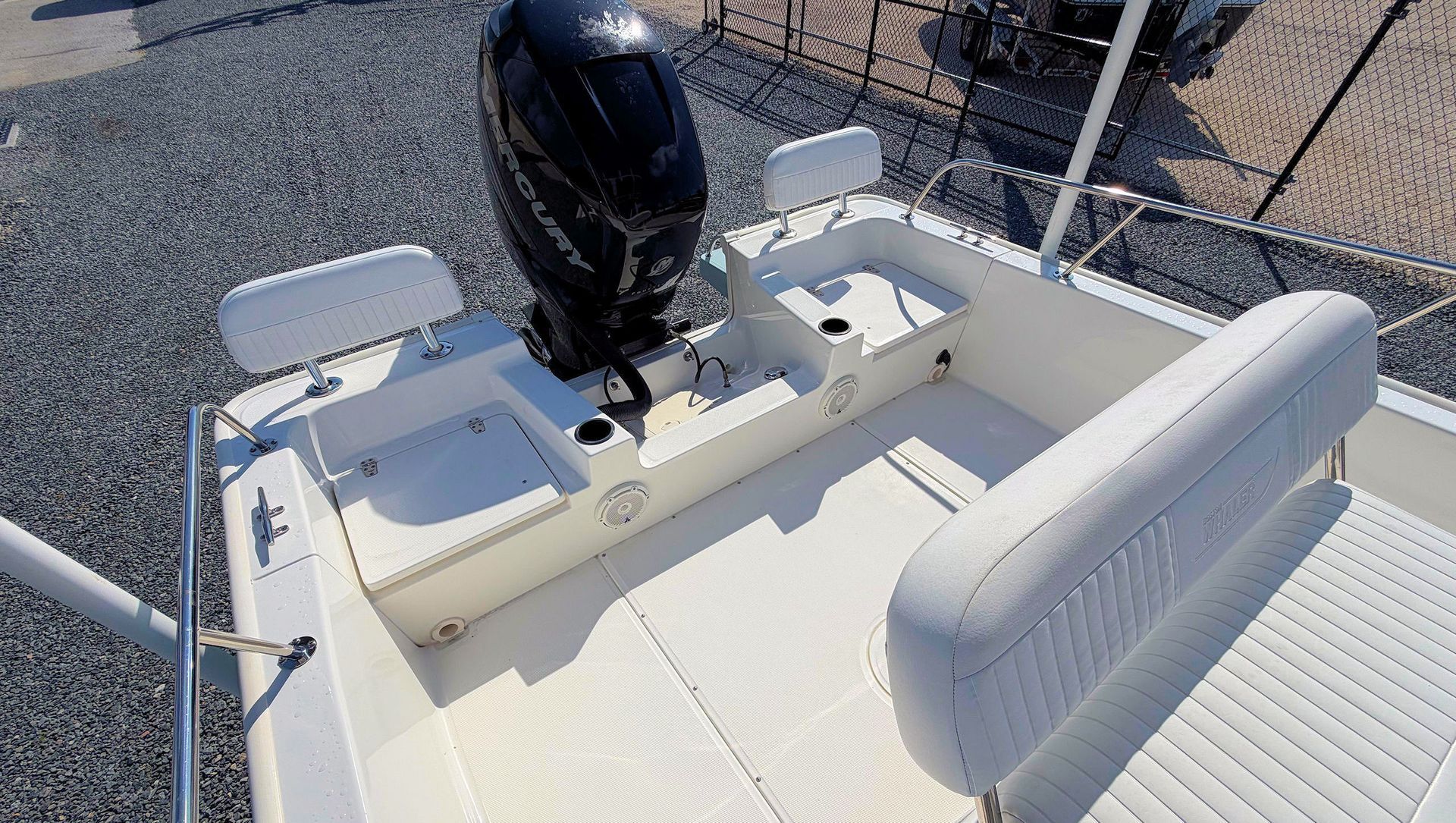 Boat cockpit with white seating and a black outboard motor on a gravel lot