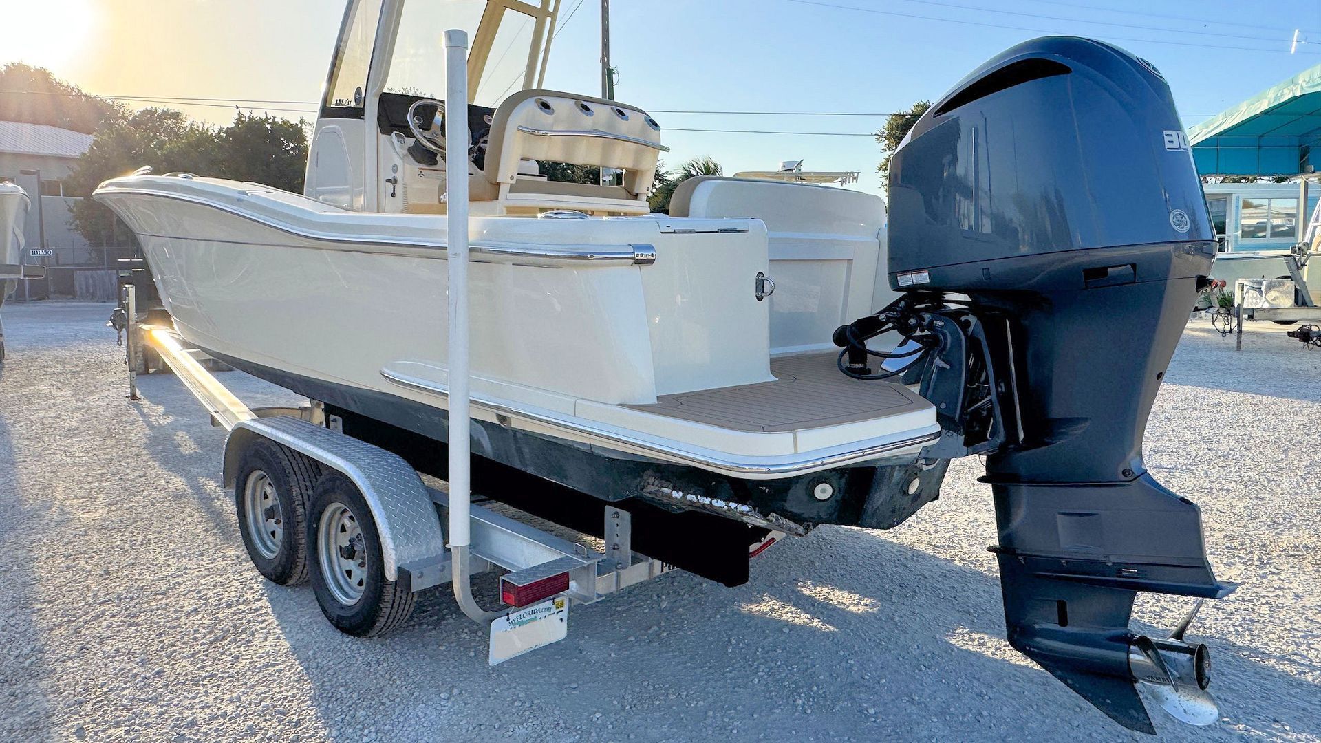 White center console boat on a dual-axle trailer with a black outboard motor in a gravel lot at sunset