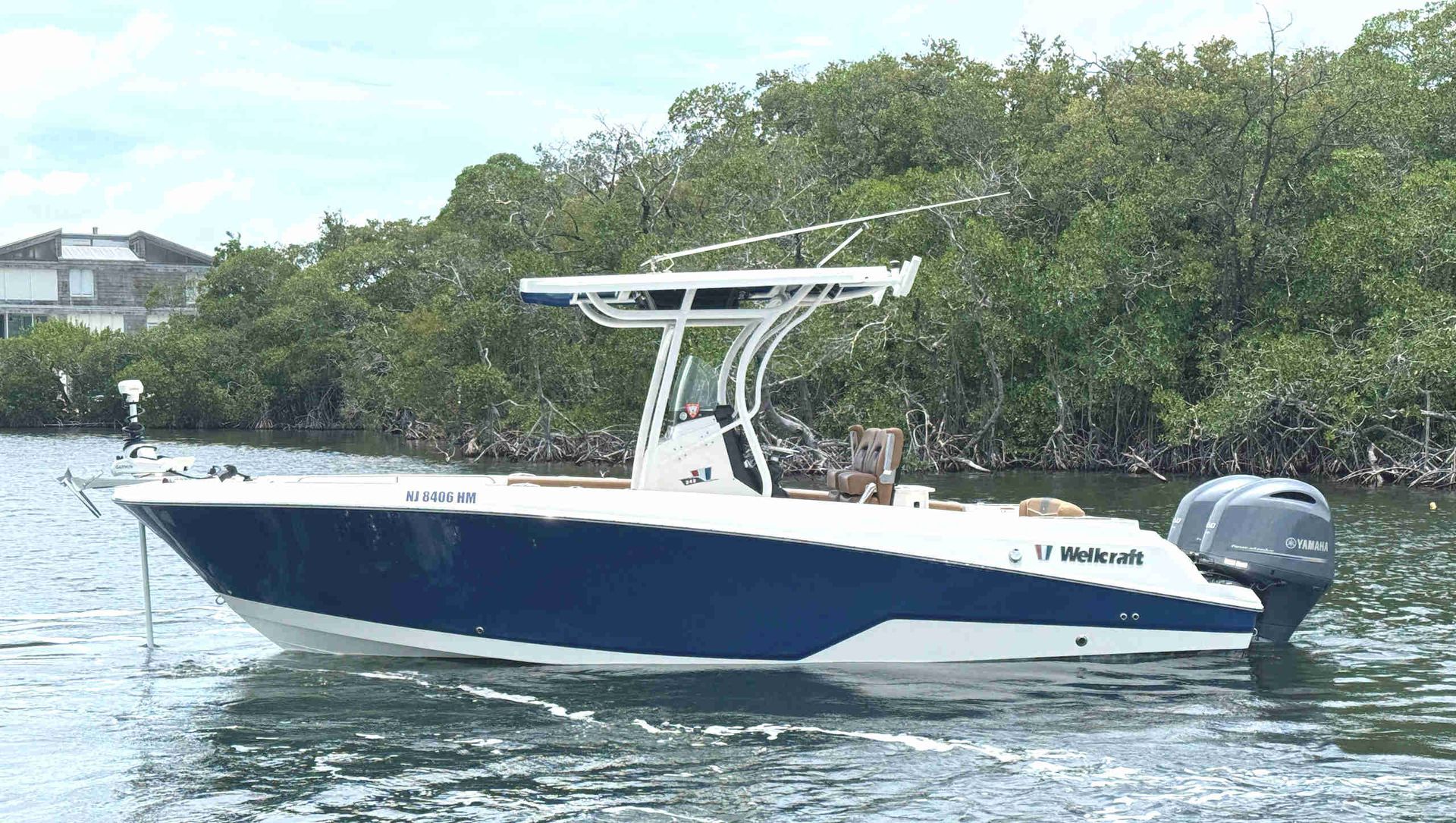 Wellcraft 242 Fisherman boat cruising on calm water near a tree-lined shore.