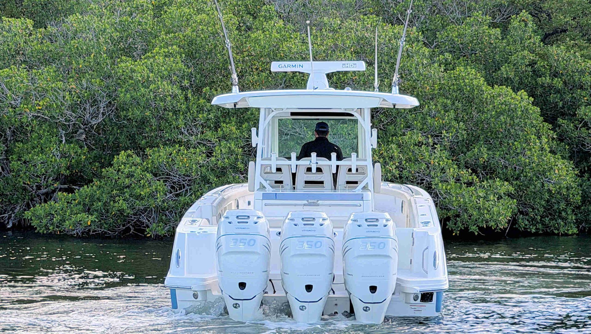White center-console boat cruising on calm water with a person at the helm, backed by dense green mangroves