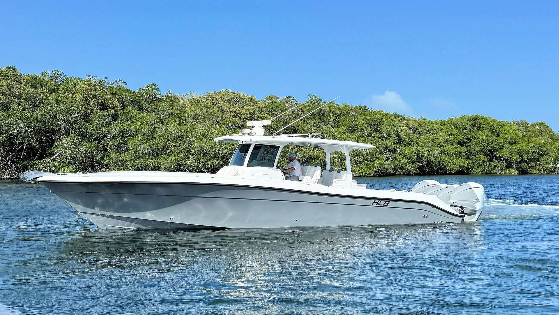 Center console fishing boat cruising on blue water near a lush green shoreline under a clear sky