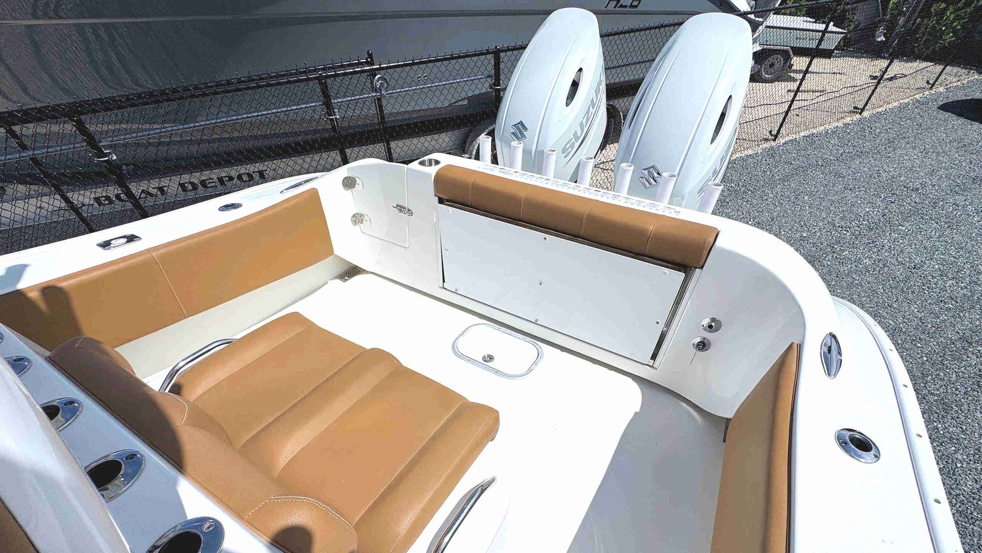 White boat cockpit with tan seats and twin outboard engines, docked on gravel near a fence.