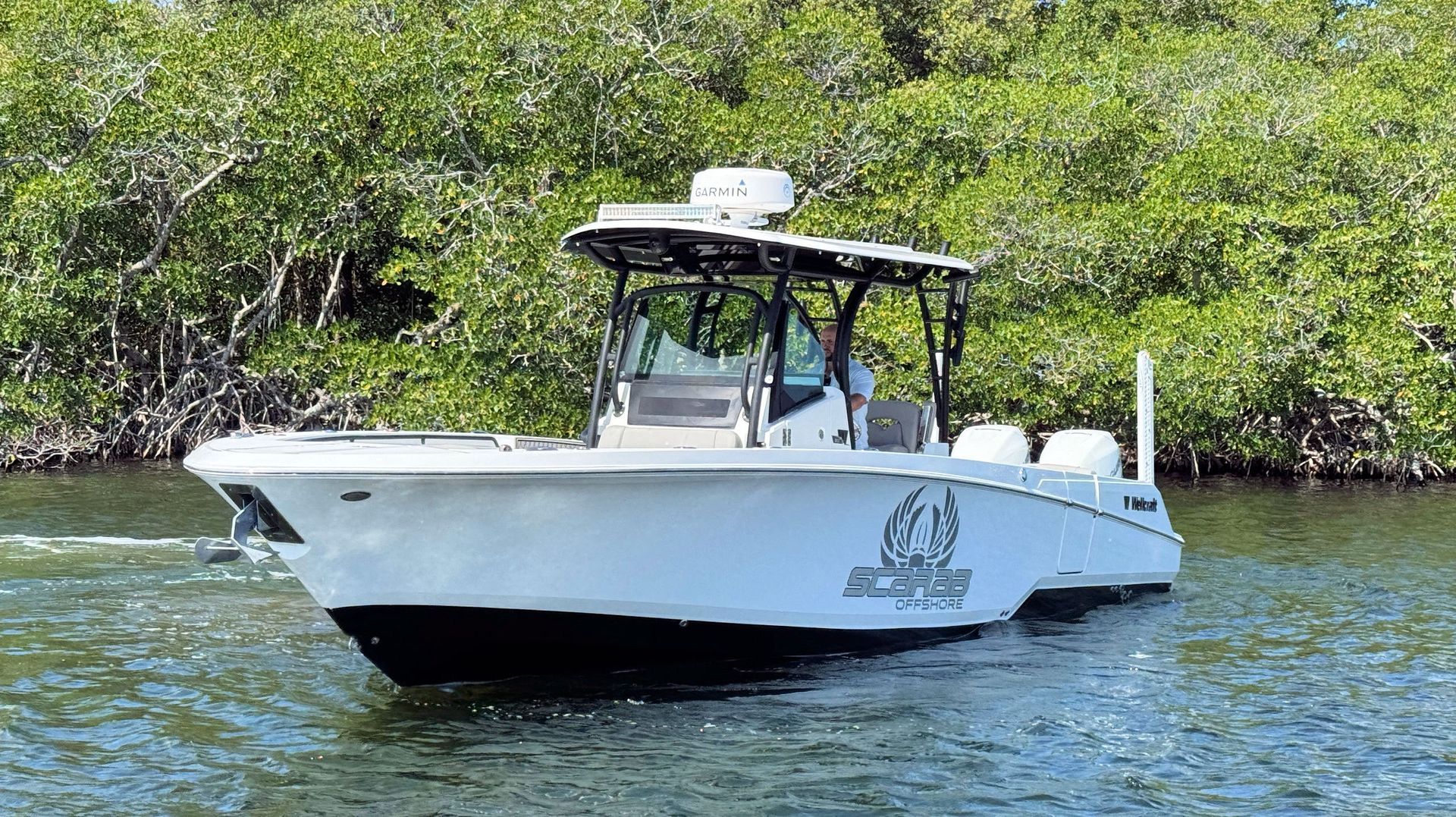 White center-console boat on calm water near mangroves, with a black canopy and people aboard.