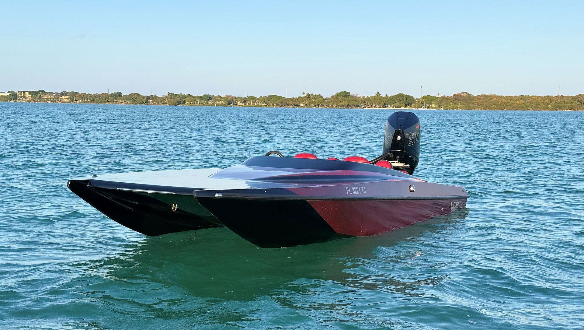 Red and black speedboat on choppy blue water near a tree-lined shore