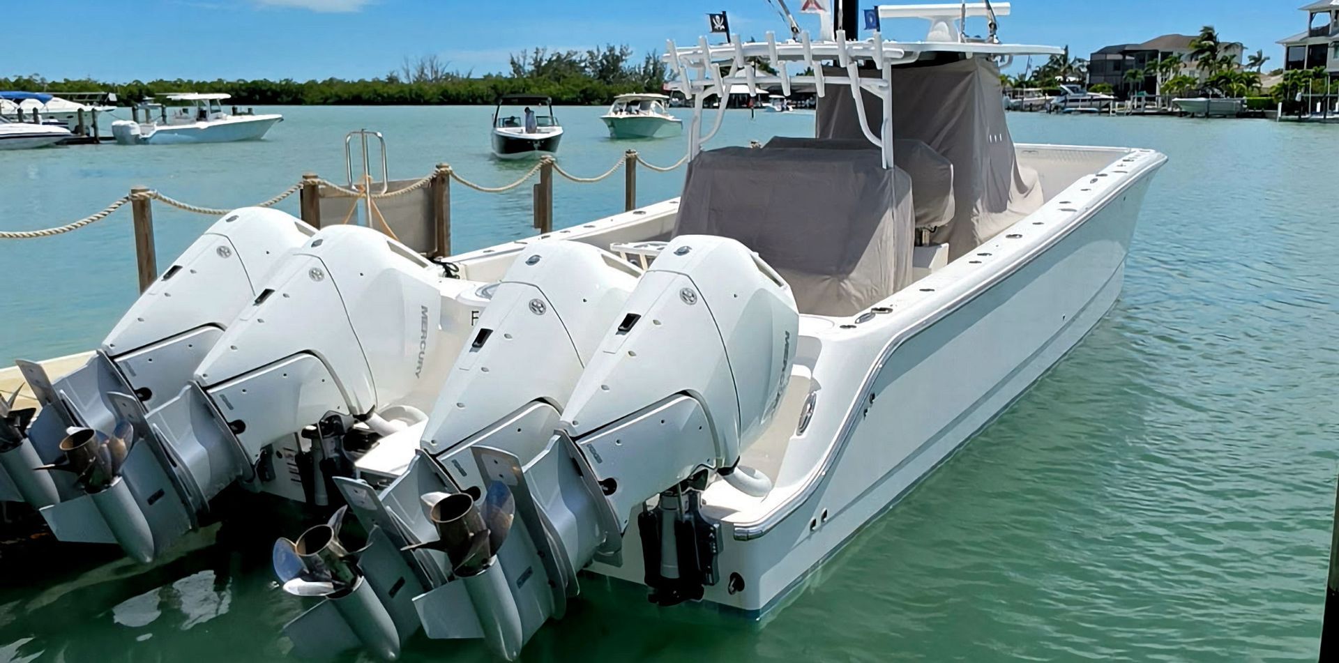 White center console fishing boat with quad outboard motors docked on calm green water near a waterfront