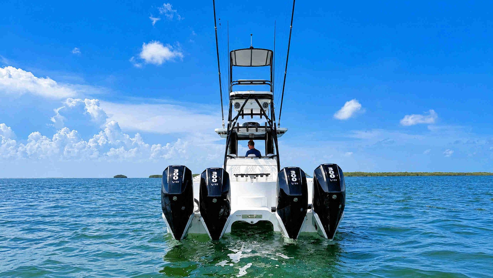White catamaran center console fishing boat with four outboard motors on blue water under a clear sky