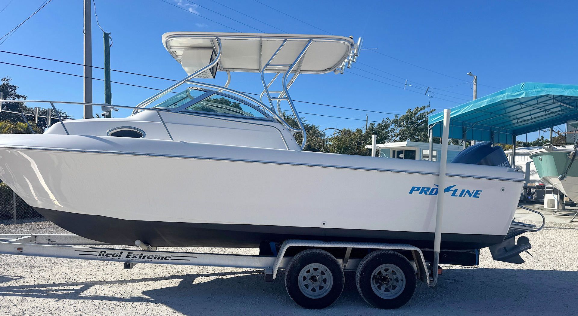 A white Pro-Line walkaround boat on a trailer parked on gravel under a bright blue sky.