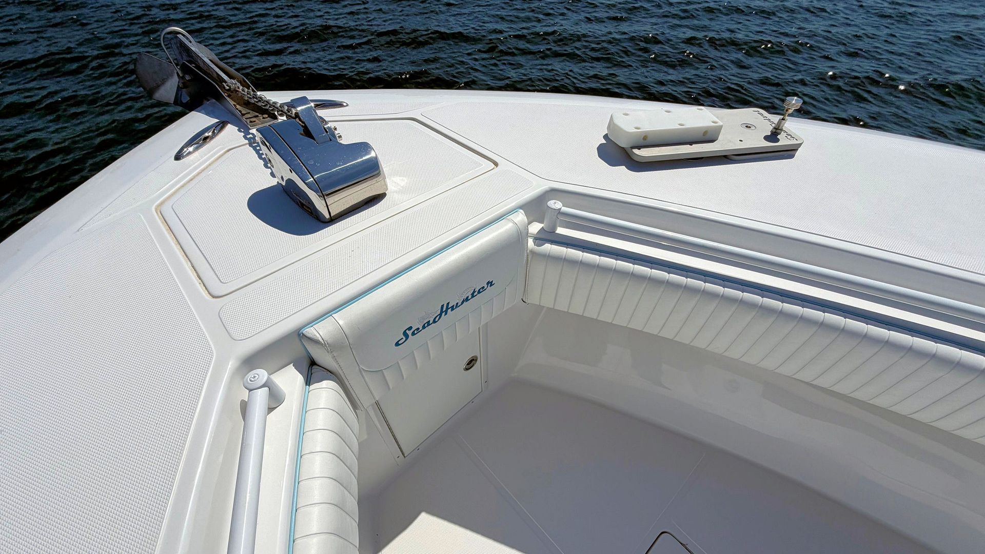 Bow of a white boat with textured deck, blue water beyond, and a metal anchor gear mounted near the edge