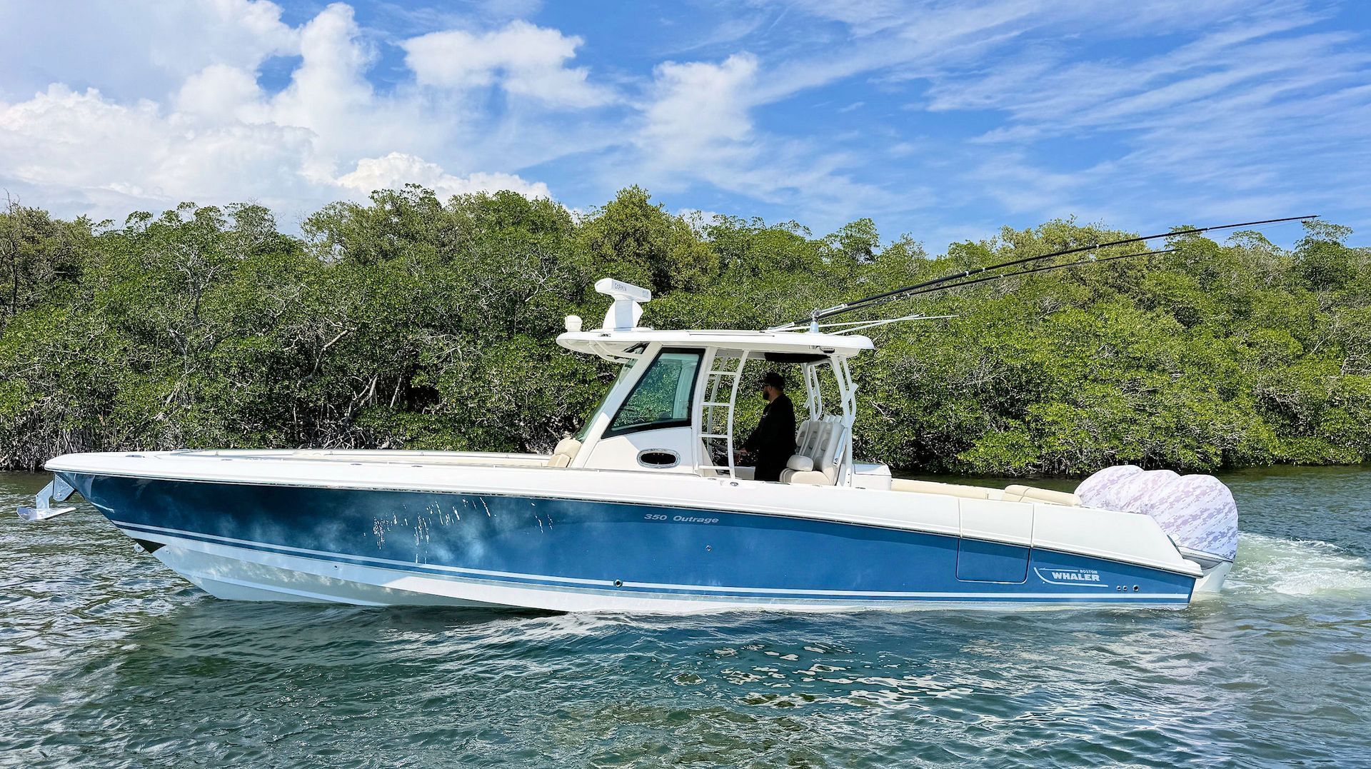 Blue-and-white center console  fishing boat on calm water near a green shoreline under a partly cloudy sky