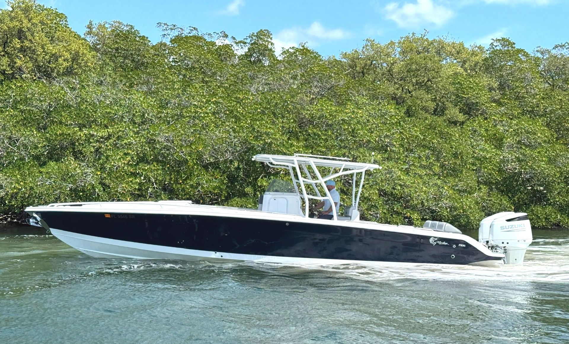 White speedboat on choppy water with a canopy, passing in front of dense green trees