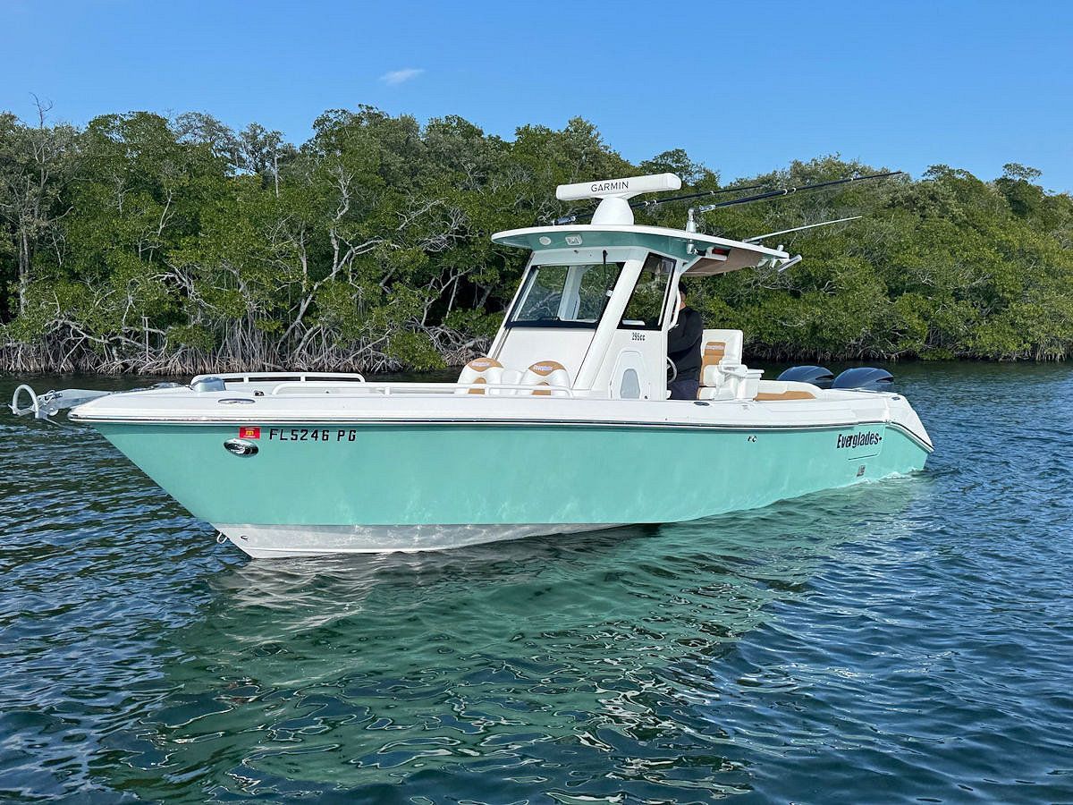 A teal and white motorboat floats in calm water near green trees.