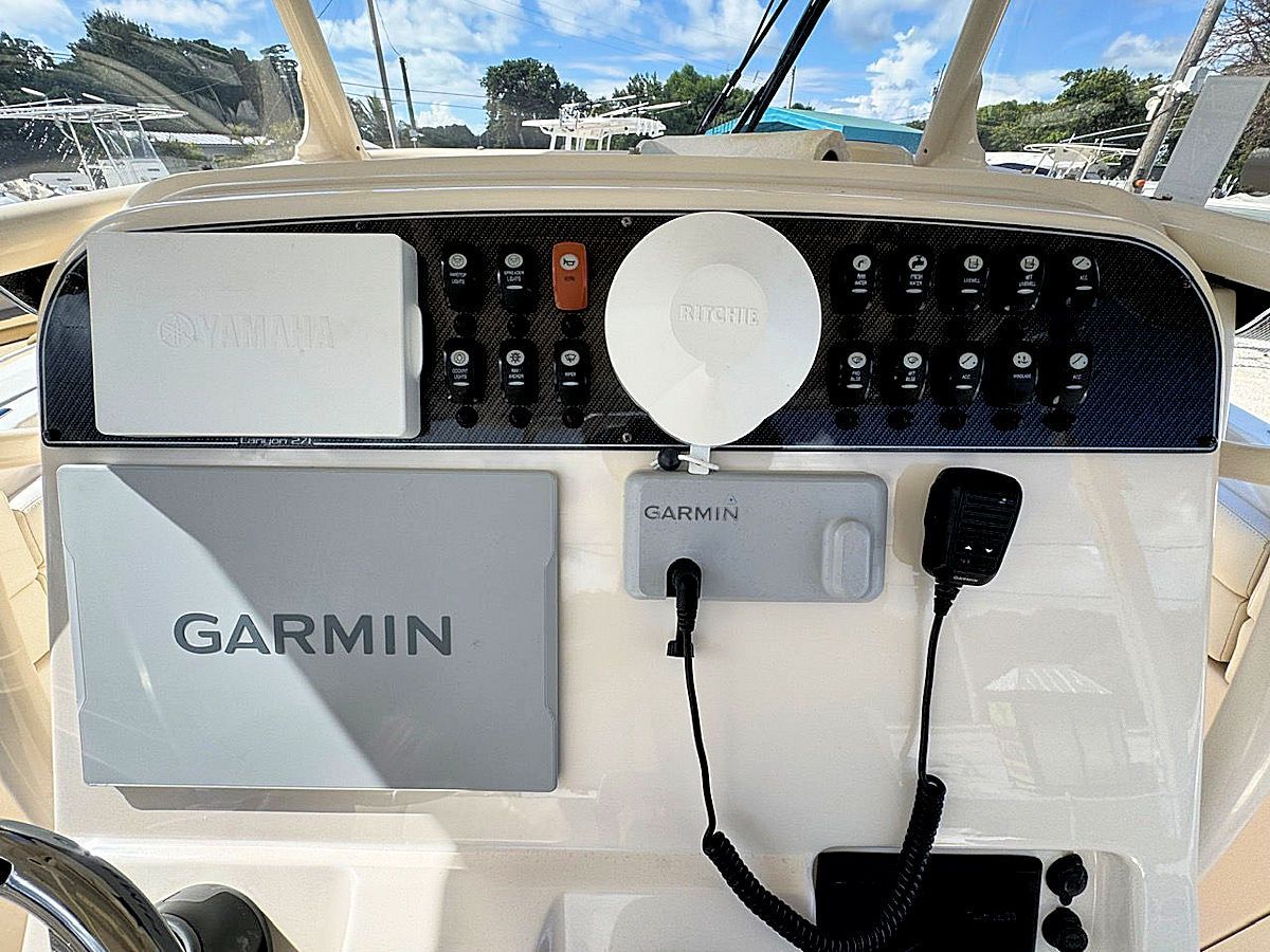 Dashboard of a boat with Garmin navigation equipment, radio, and control switches, under a sunny sky.