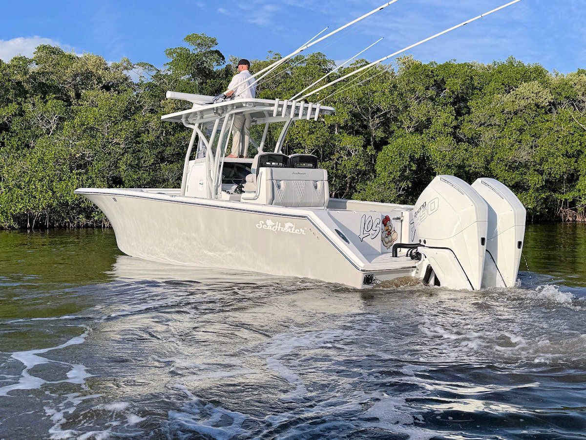 A white fishing boat with two engines on the water near mangroves, person stands on a tower.