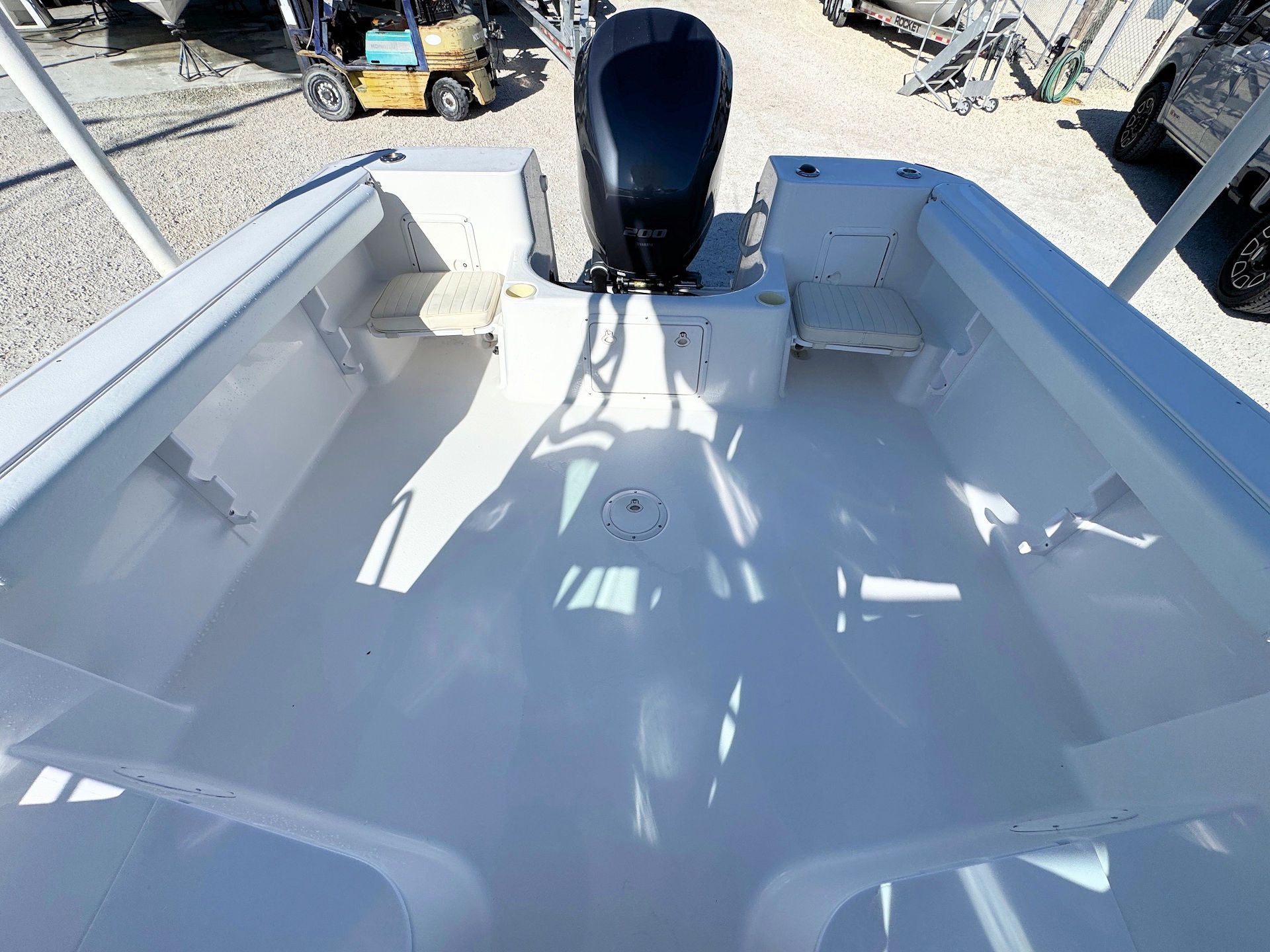 The interior stern of a white boat, showing rear jump seats and a black outboard motor, parked on a gravel lot.
