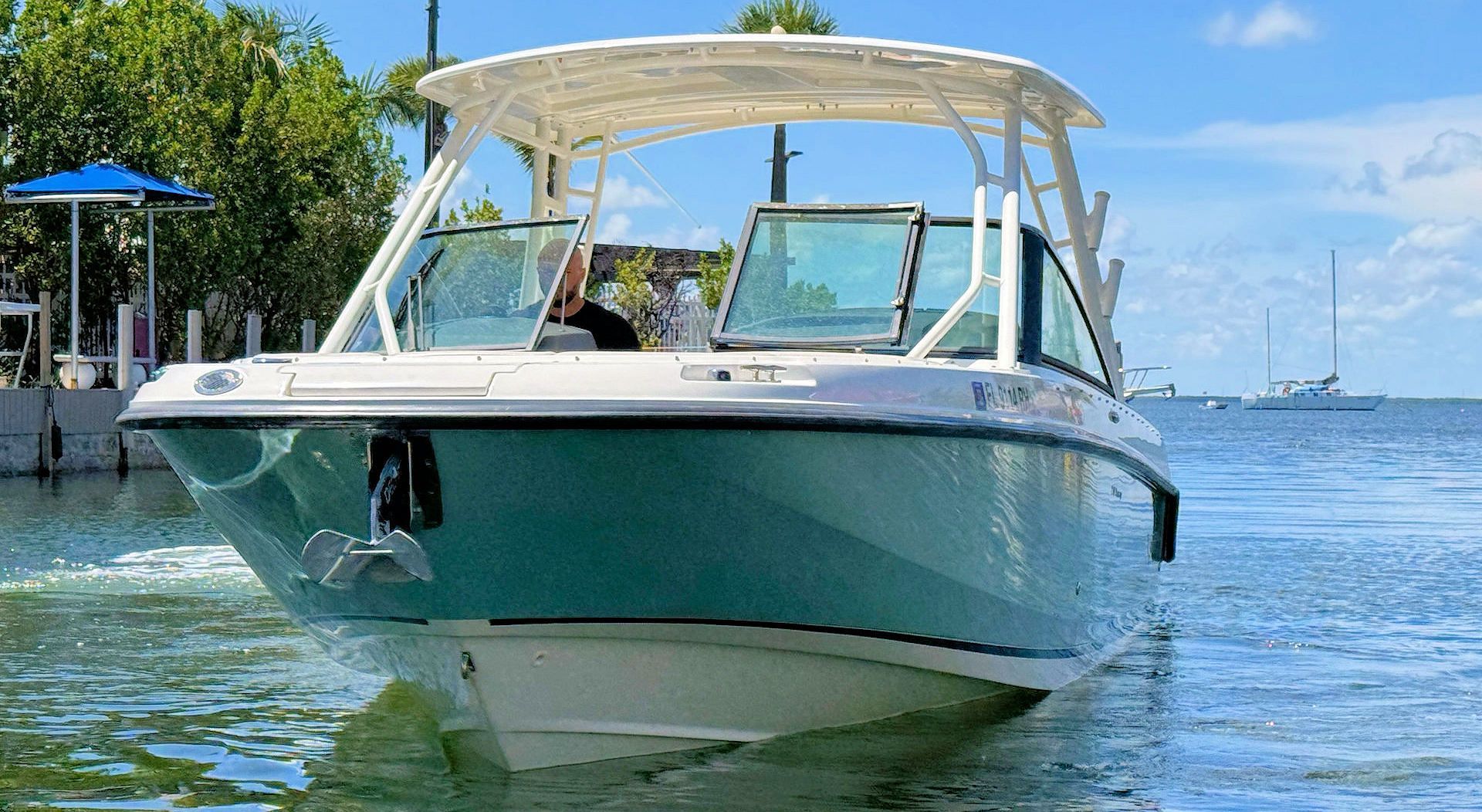 A light blue and white dual-console powerboat on calm water with a sunshade, moored near a pier under a sunny blue sky.