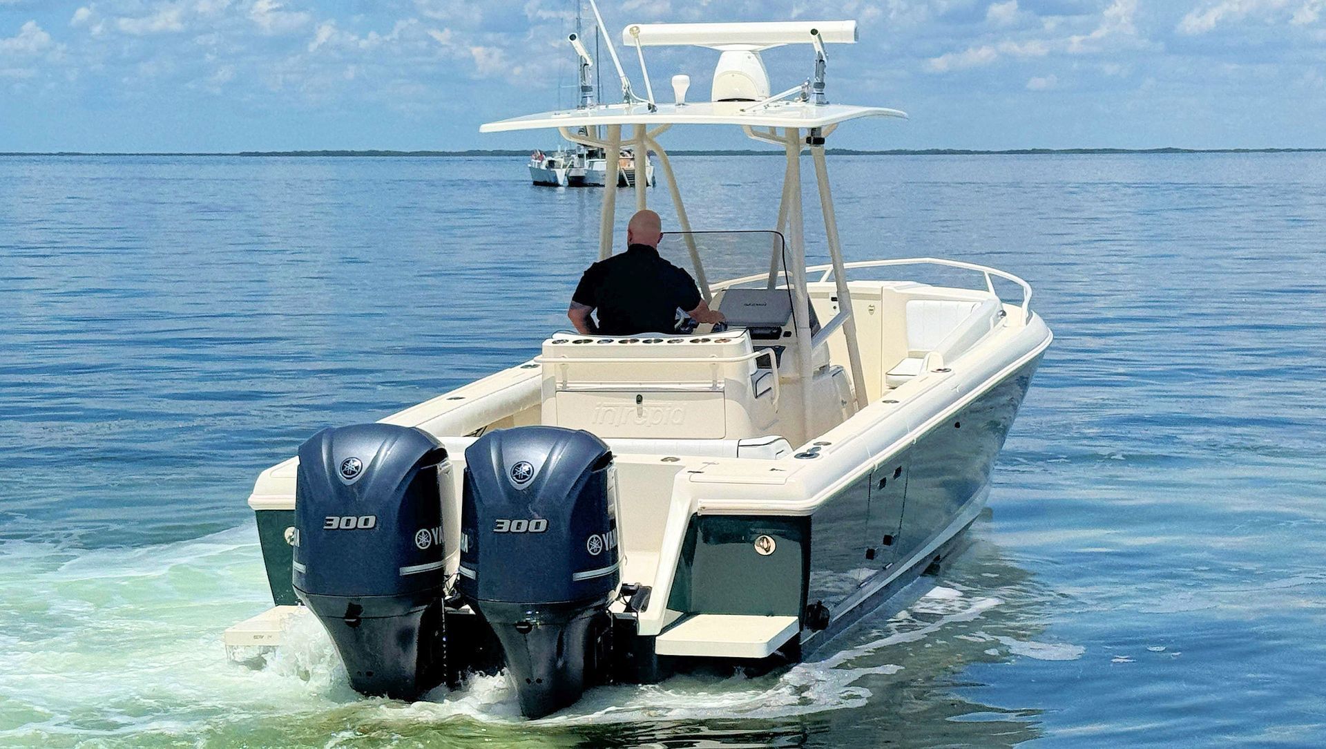 White and navy center console boat with twin Yamaha engines on calm ocean water under a clear sky