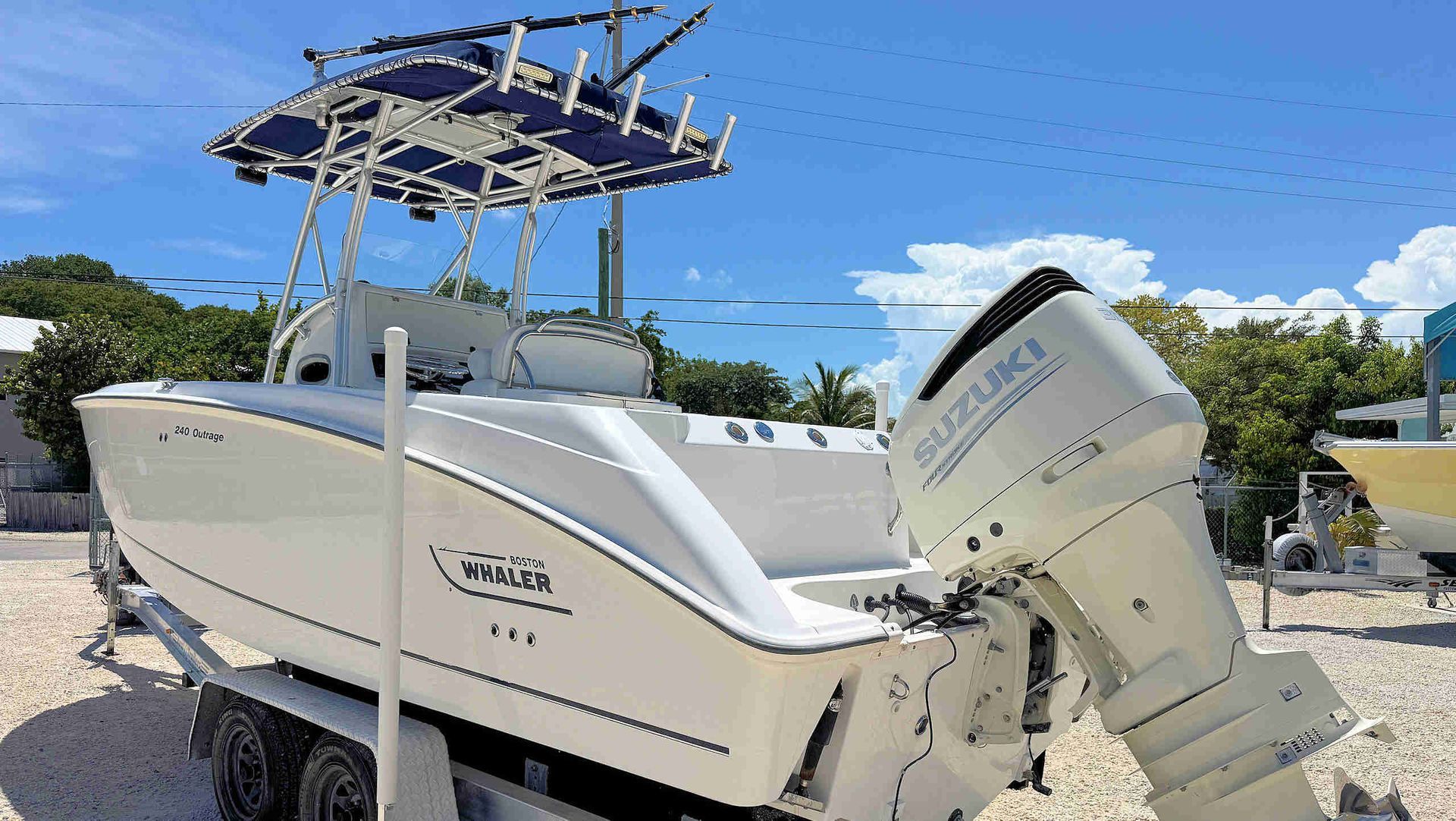 White center console boat on a trailer with a T-top and outboard engine parked under a bright blue sky.