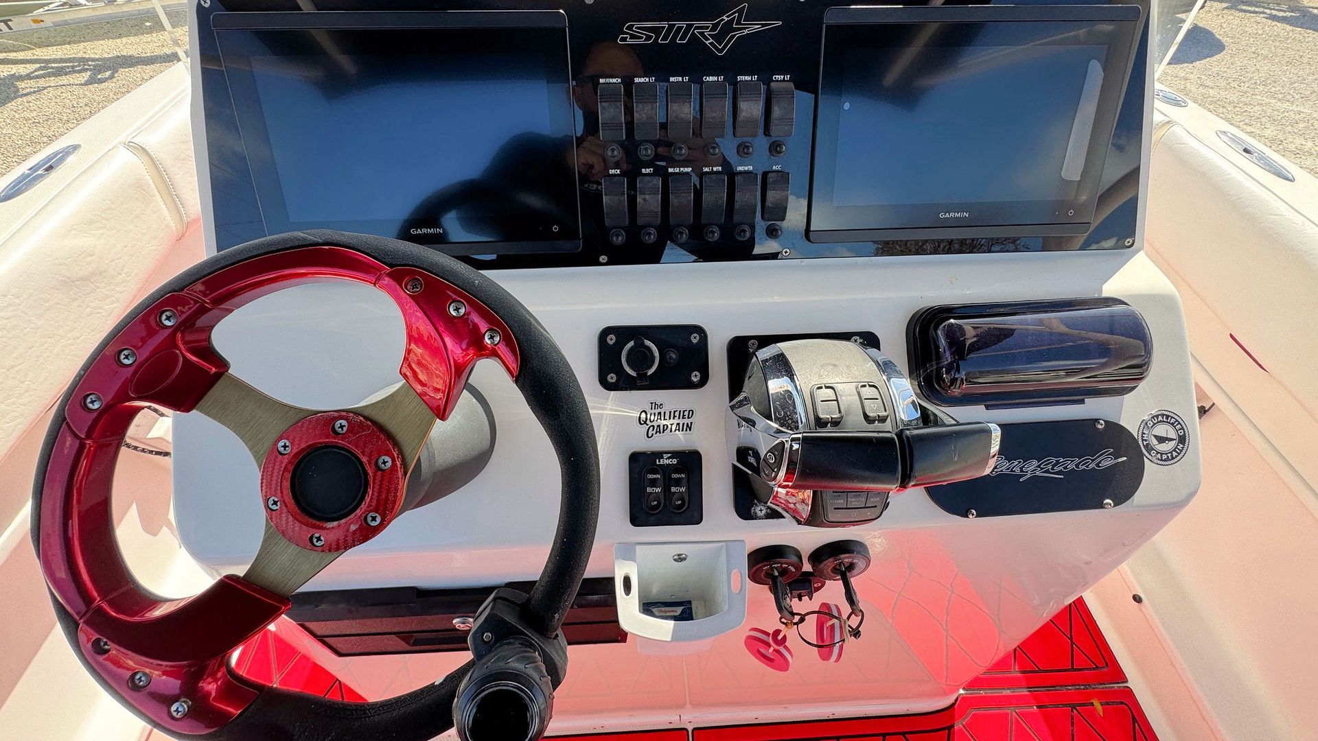 Boat helm with red steering wheel, control panel, throttle, and dark windshield under a white console
