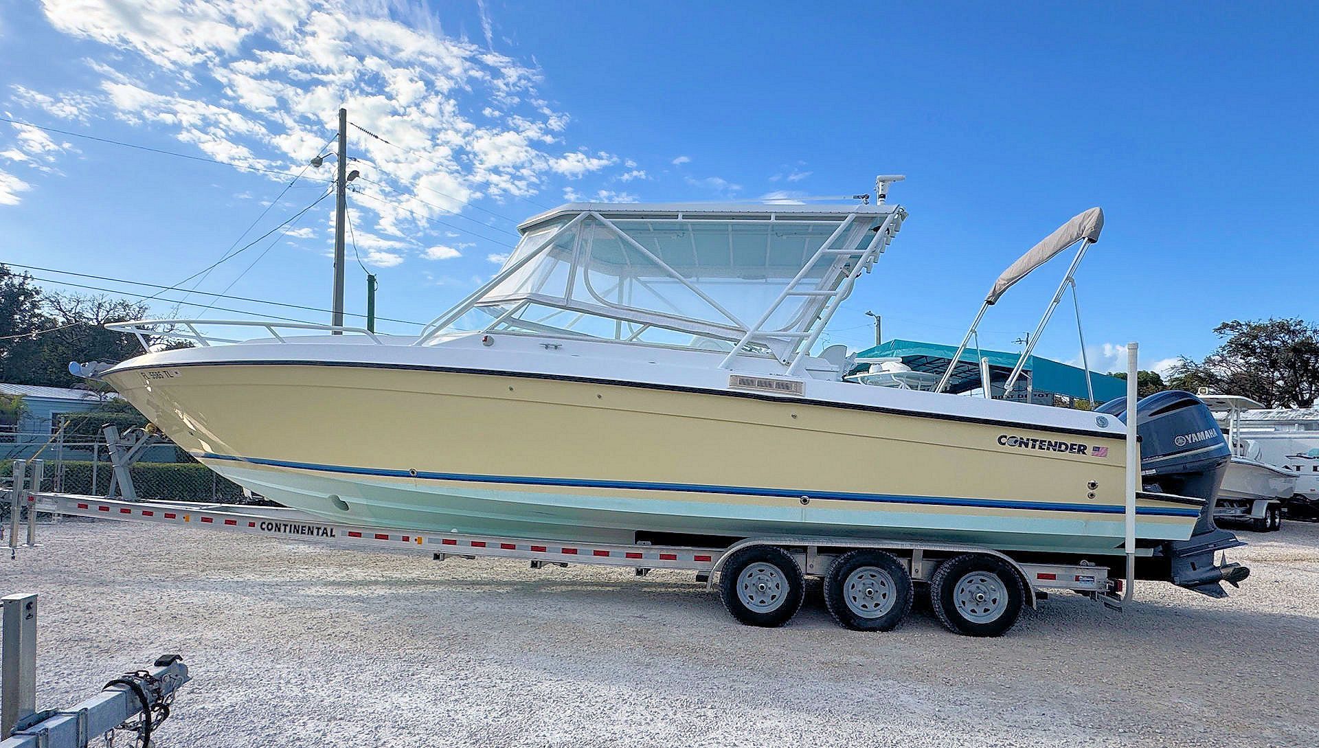 Yellow and white side-console boat on a trailer in a gravel lot under a clear sky