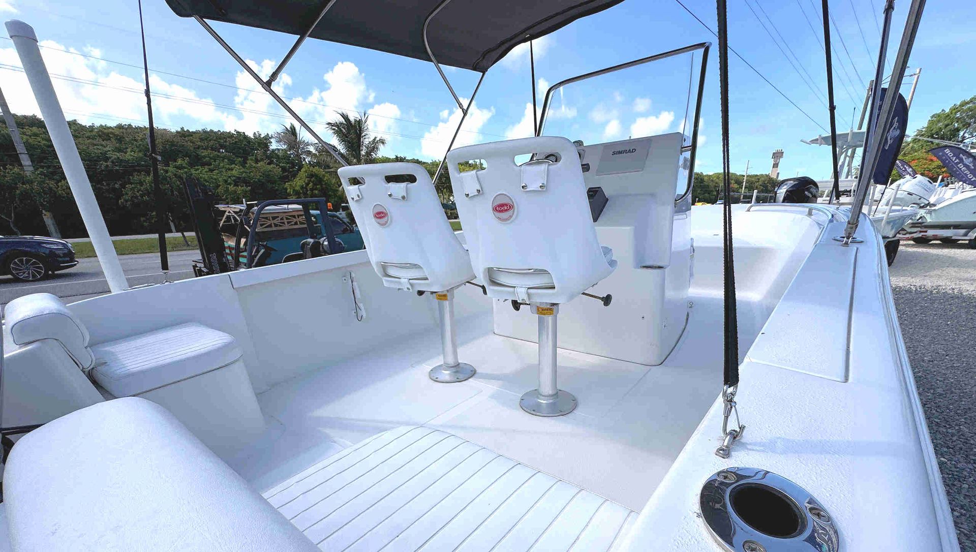 White sailboat cockpit with two swivel captains chairs, blue water, and docked shoreline in the background