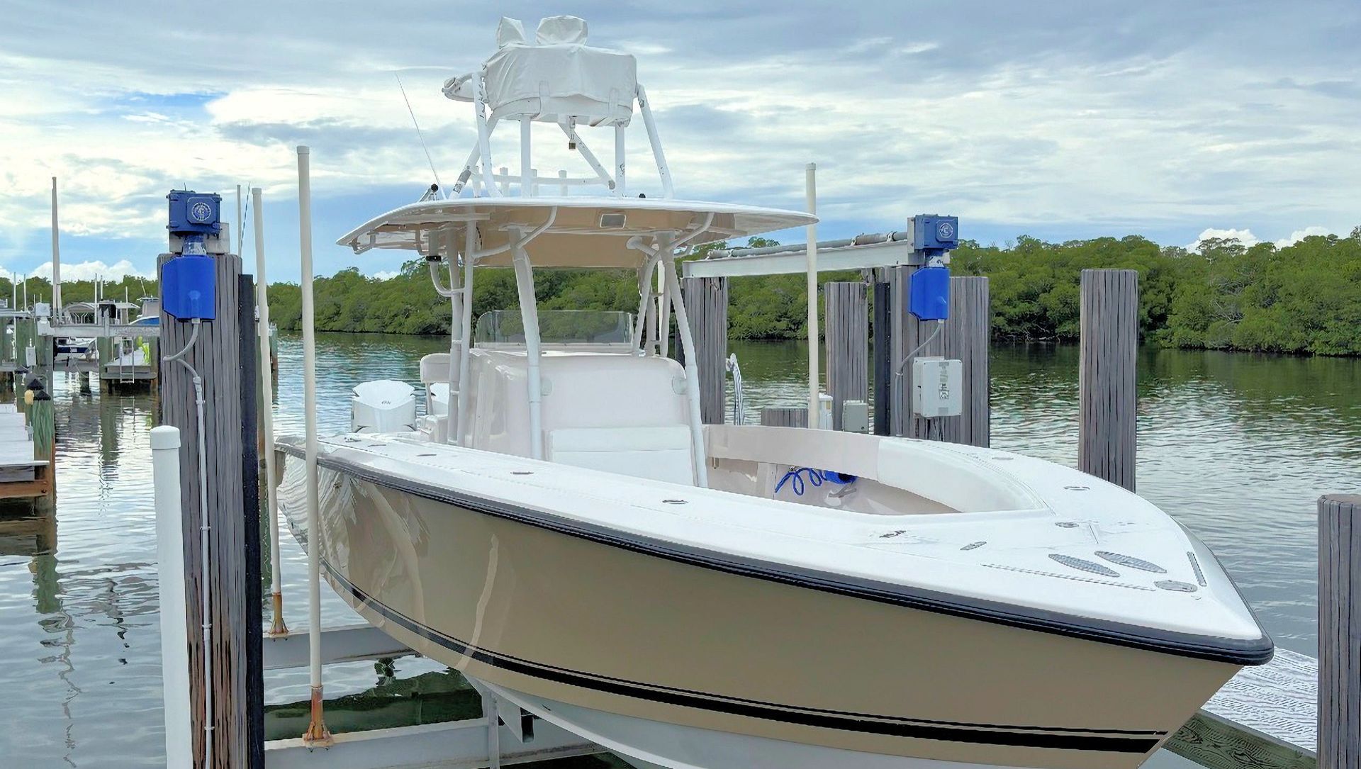 White and yellow center console fishing boat in a boat lift, with blue sky and calm water in the background