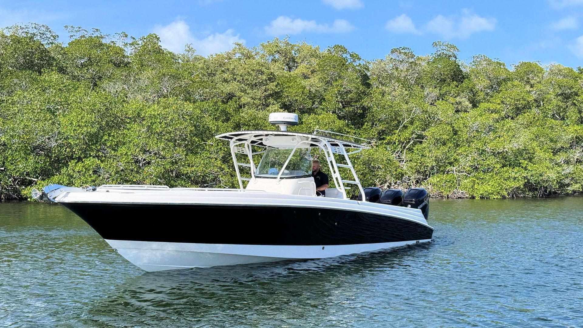 White Wellcraft center console boat cruising on calm water near a green mangrove shoreline under a blue sky