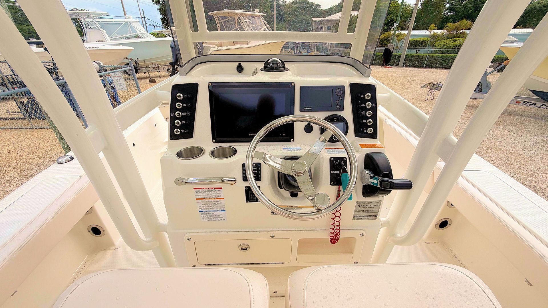 Boat helm with steering wheel, gauges, and controls in a white cockpit, facing the water.
