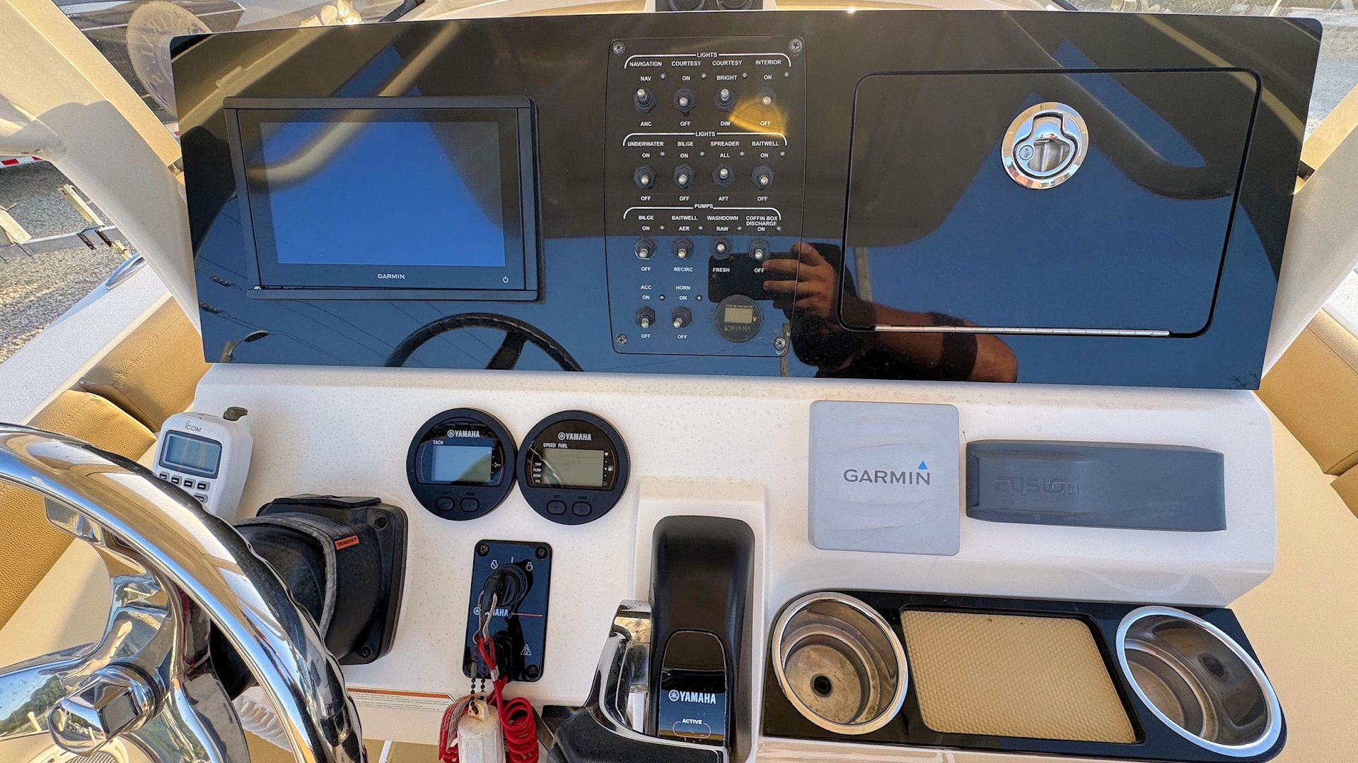 Boat helm dashboard with navigation screens, gauges, controls, and a steering wheel in bright sunlight