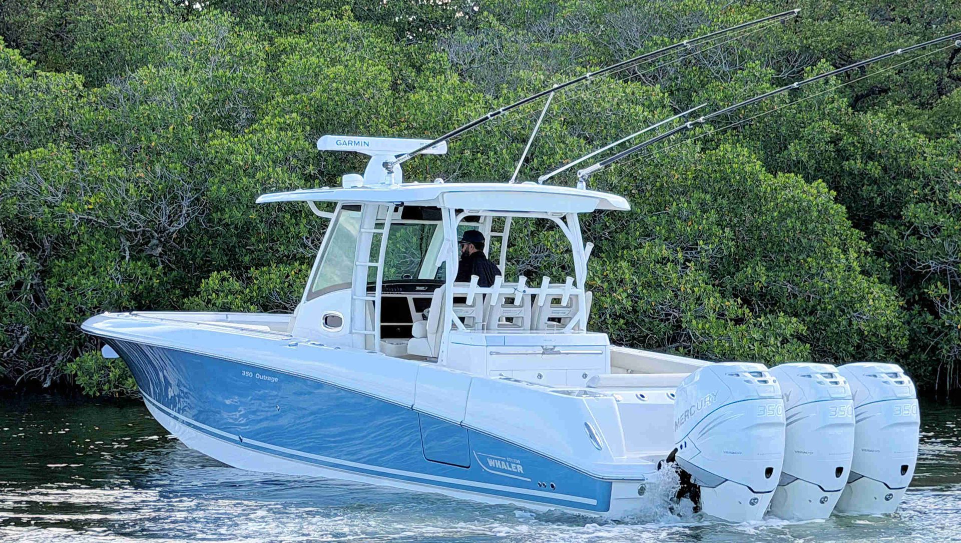 White center-console fishing boat cruising on calm water beside mangrove-lined shore