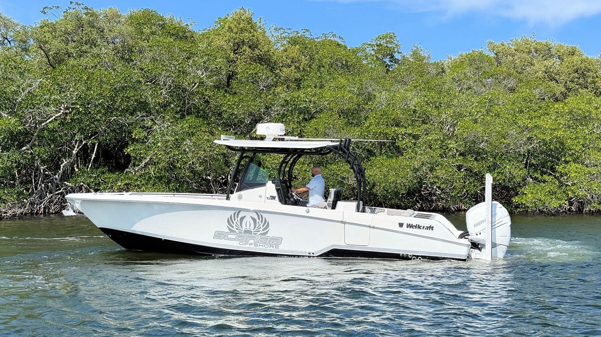 White motorboat cruising on clear water near mangrove shoreline under a blue sky