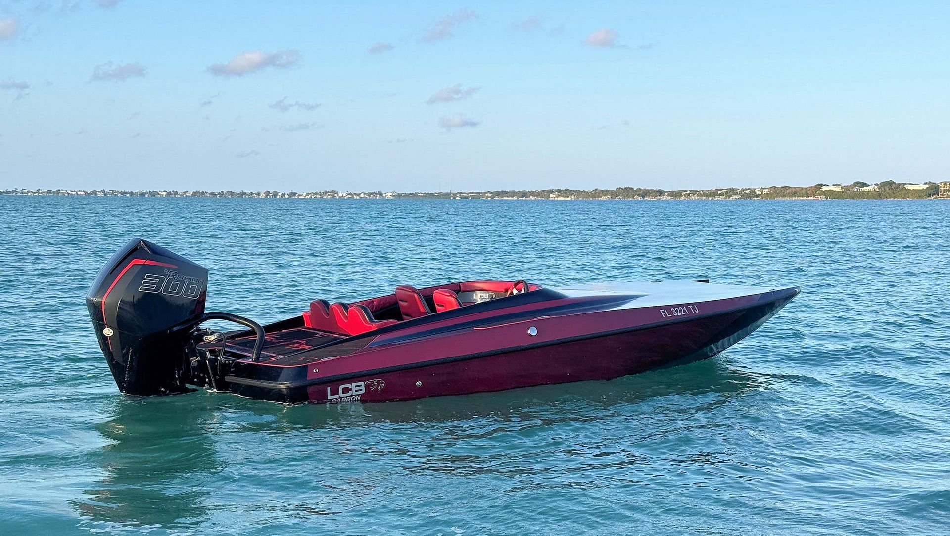 Red high-performance catamaran on choppy blue water near the shoreline under a clear sky