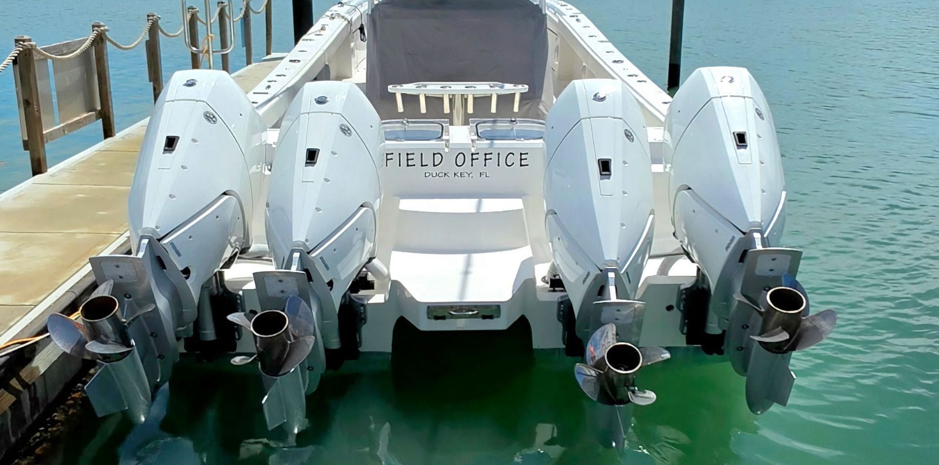 White center console fishing boat docked on turquoise water, stern facing the pier.