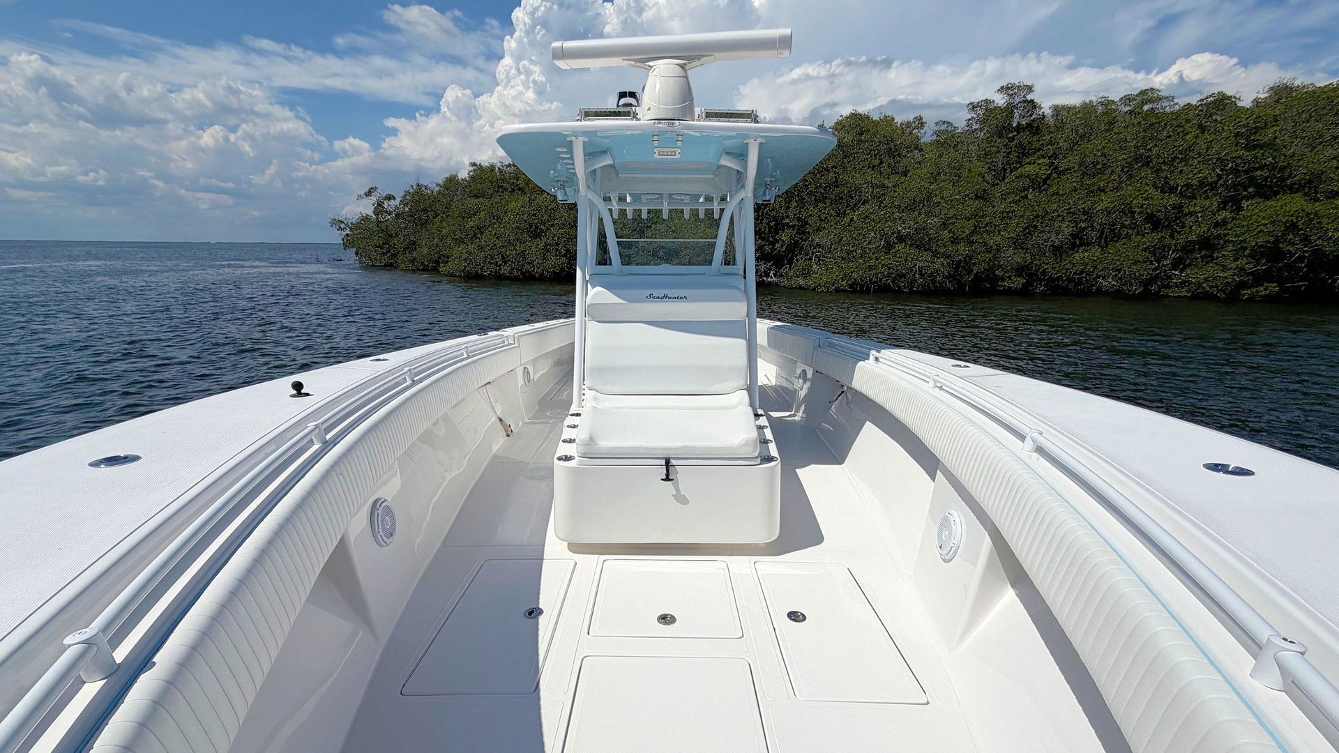 View from a white boat’s bow toward a tropical island and blue ocean under a partly cloudy sky