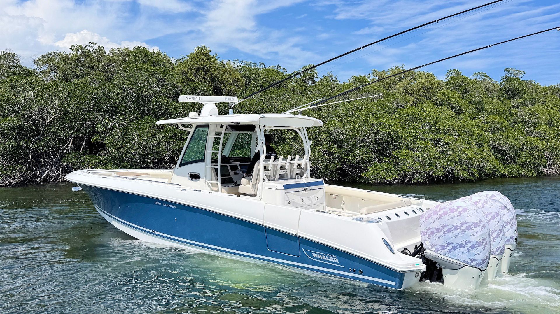 Blue-and-white center-console boat cruising on calm water near mangroves under a clear sky