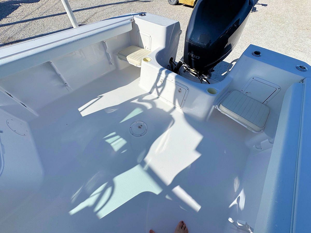 White boat interior with seats, motor, and various storage compartments. Sunny outdoor setting.