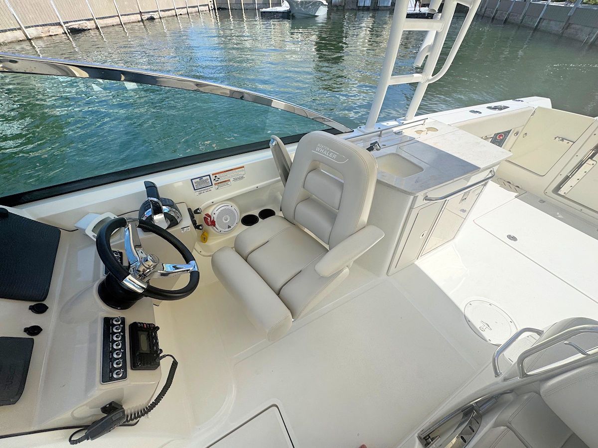 Boat cockpit with steering wheel, seat, and console. Bright, sunny day.
