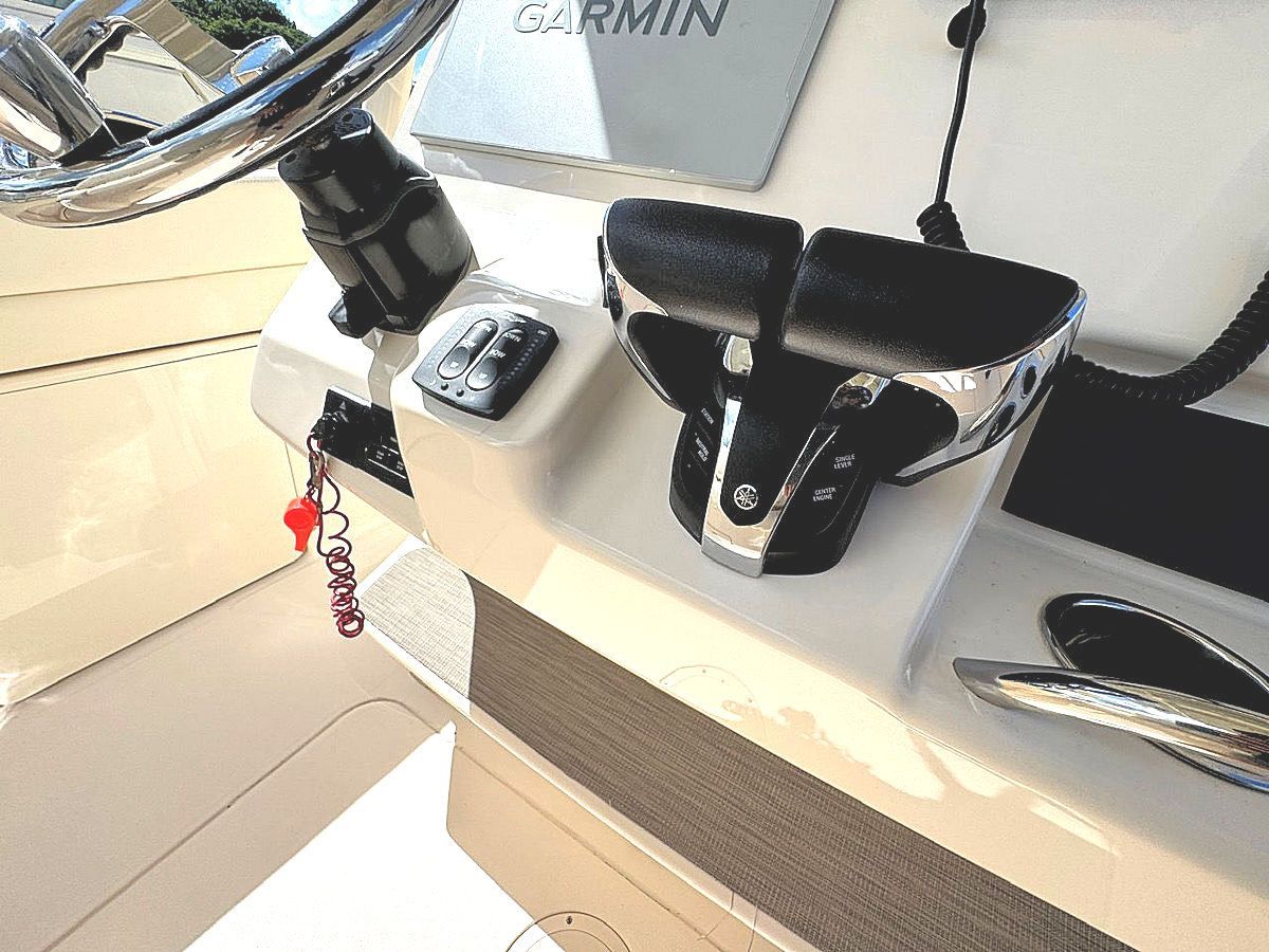 Boat dashboard with a steering wheel, Garmin display, and controls. White and gray tones.