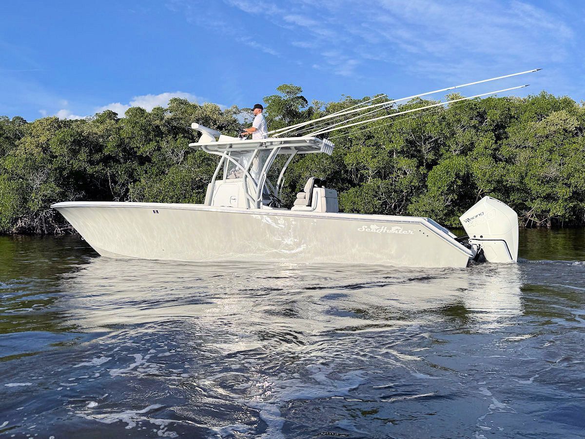 Boat with fishing rods on water, person at helm, mangroves in background, sunny day.
