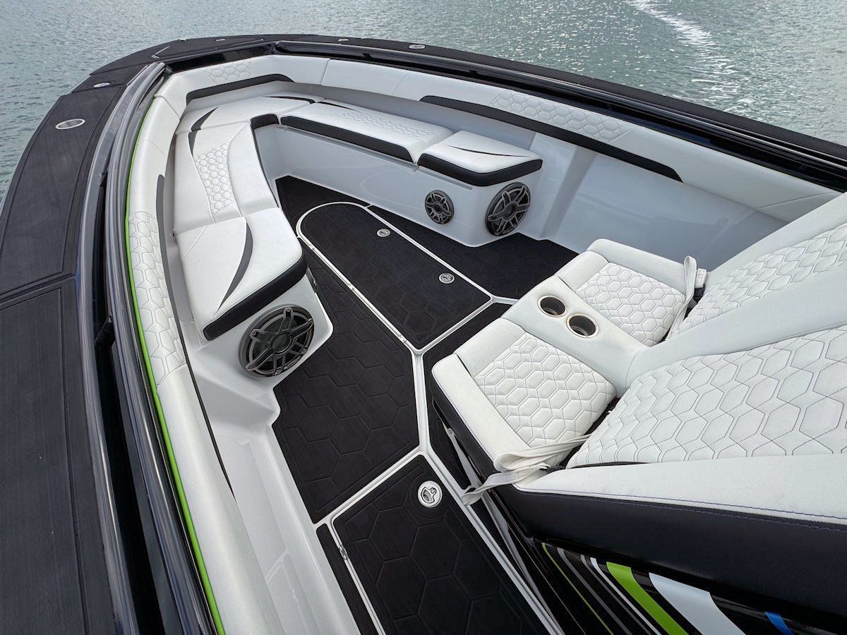 Interior of a boat with black and white seats and flooring, and speakers.