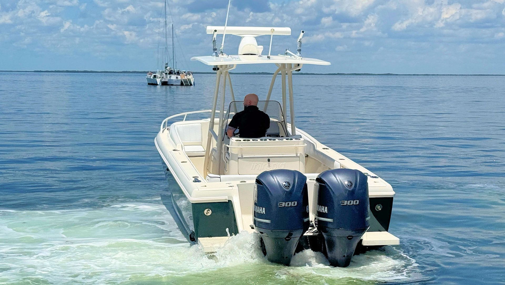 White and navy center console boat speeding on calm blue water, viewed from behind, with twin outboard engines
