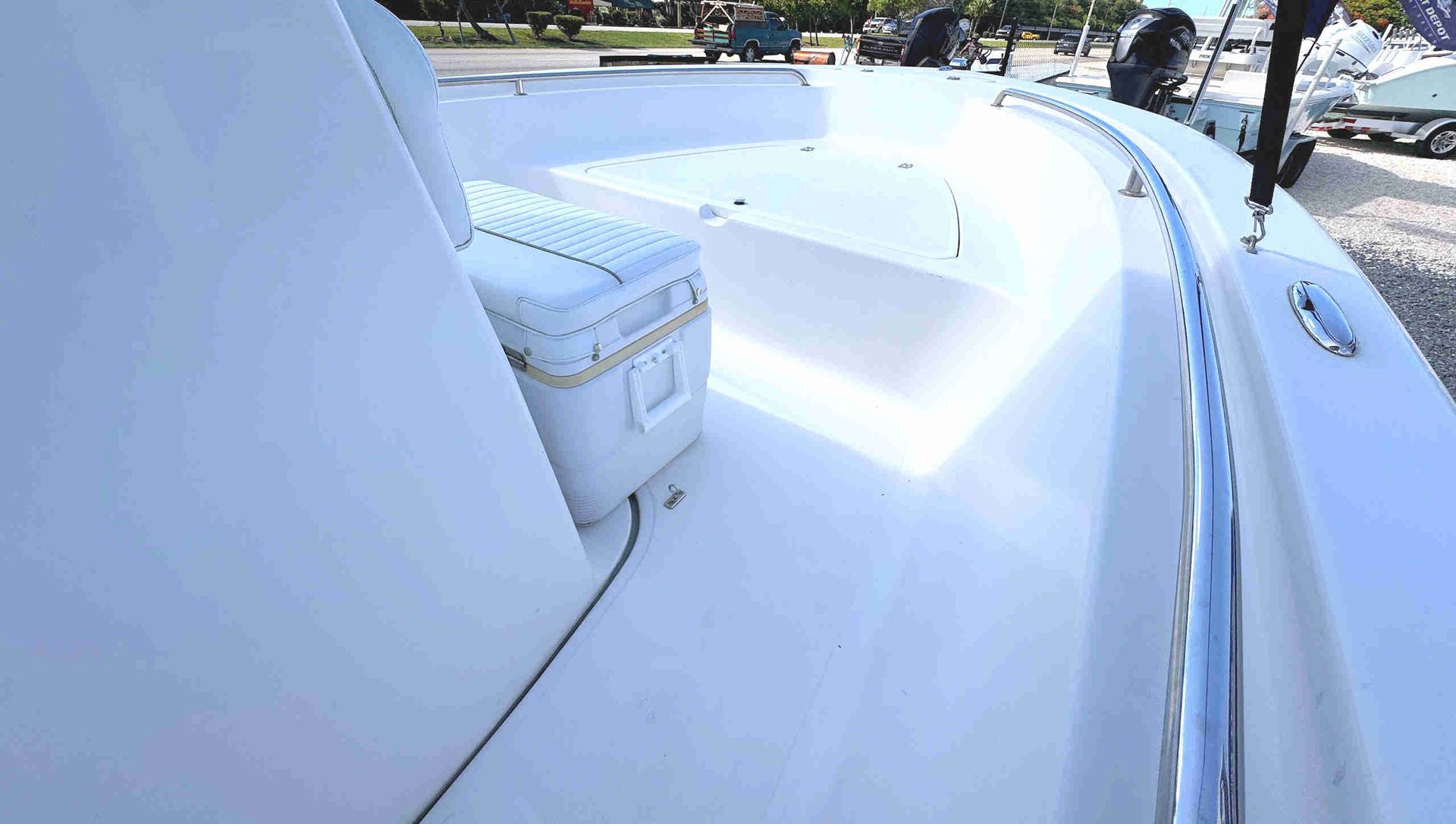 White boat deck with an ice box with cushioned lid, curved railing, and bright sunlight on the water.