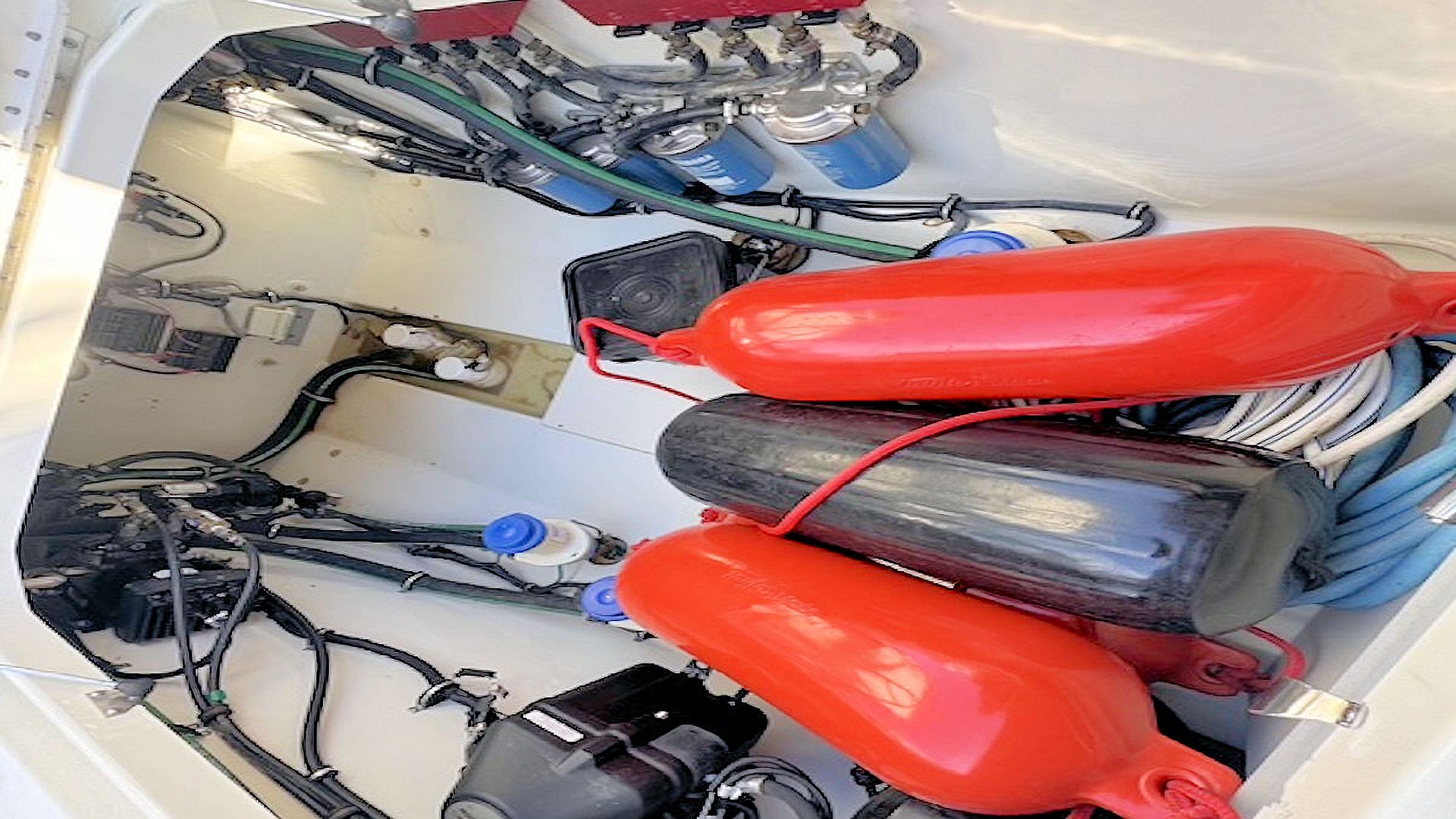 Two red fenders stored side by side in a narrow white compartment with coiled ropes and gear