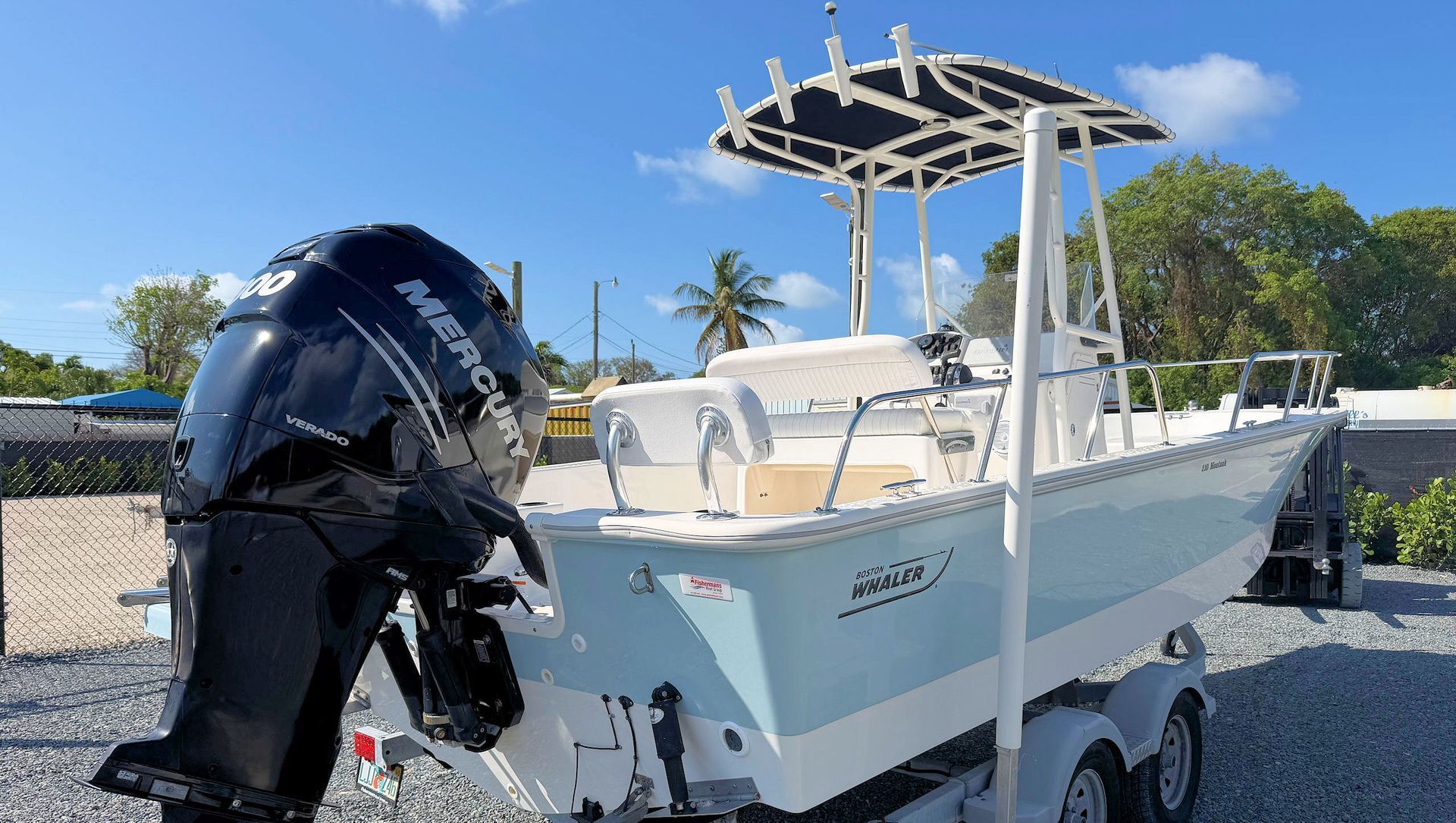 White center-console boat on a trailer with black outboard motor, parked outdoors under a blue sky