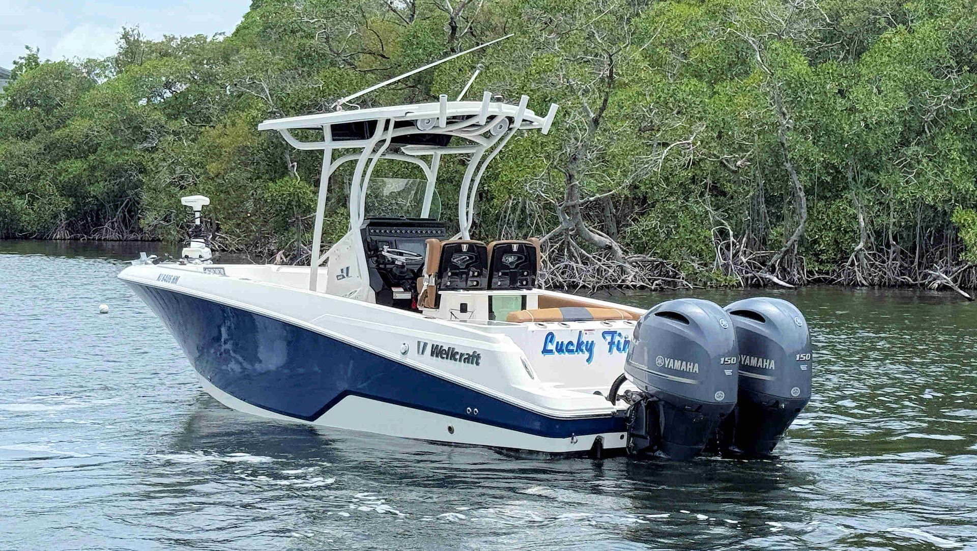 Wellcraft 242 Fisherman boat with twin outboard motors floating on calm water near mangrove shoreline.