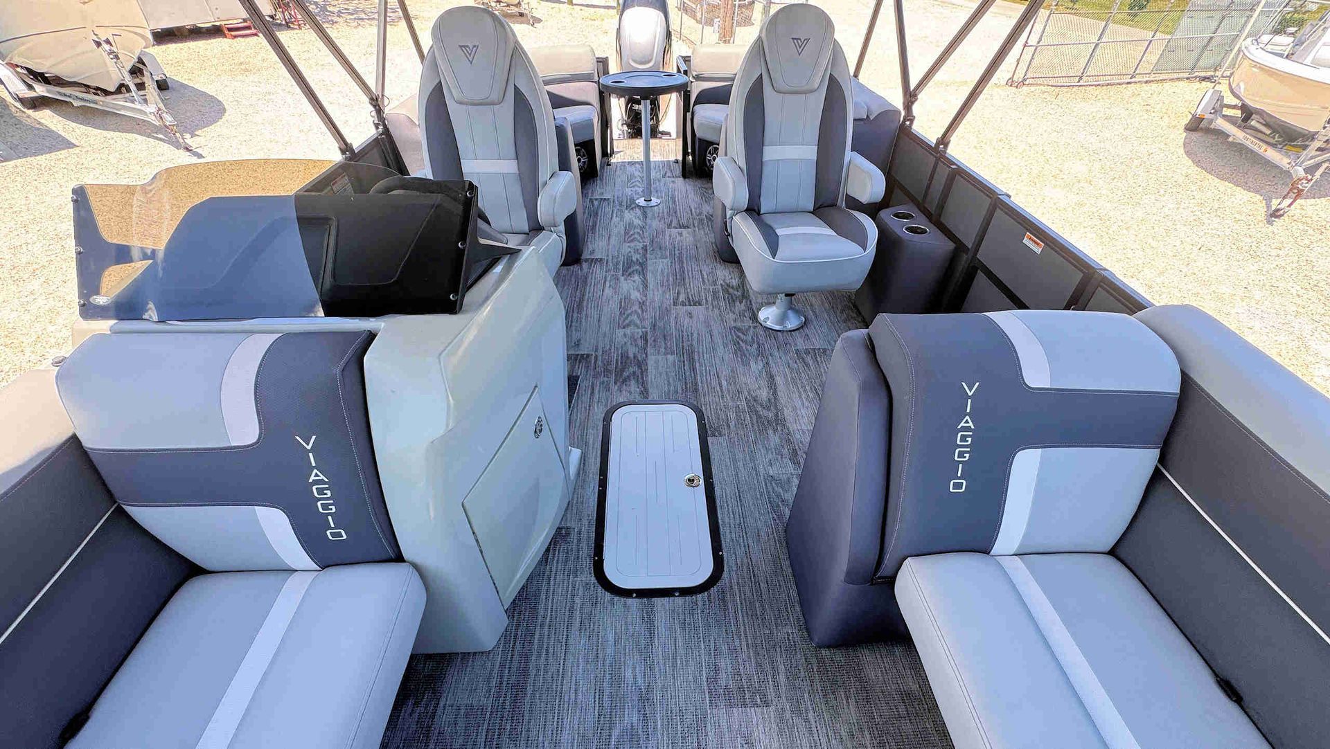 Tritoon boat interior with gray cushioned seats, central aisle, and a small table in bright sunlight