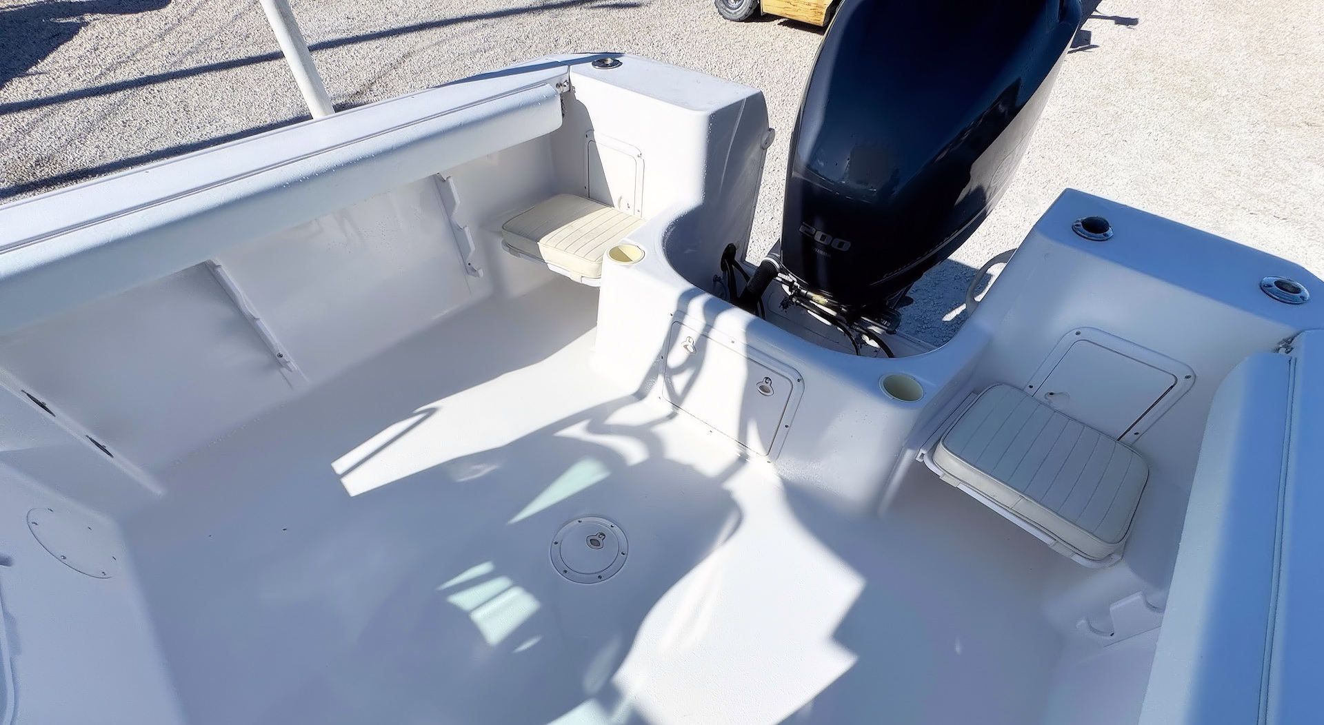 The rear deck of a white boat featuring two fold-down jump seats, a central floor drain, and a mounted black outboard motor.