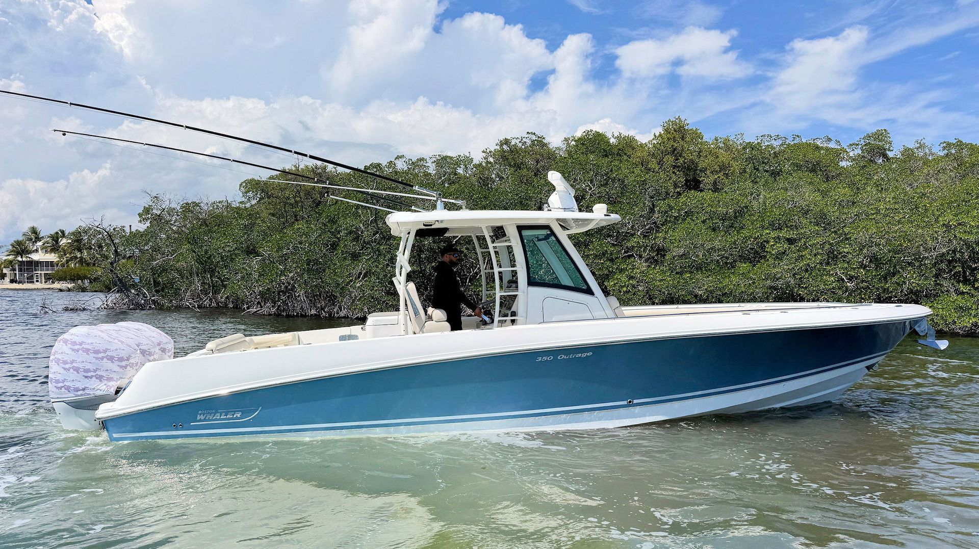 Blue and white center console  fishing boat on calm water near mangroves under a partly cloudy sky