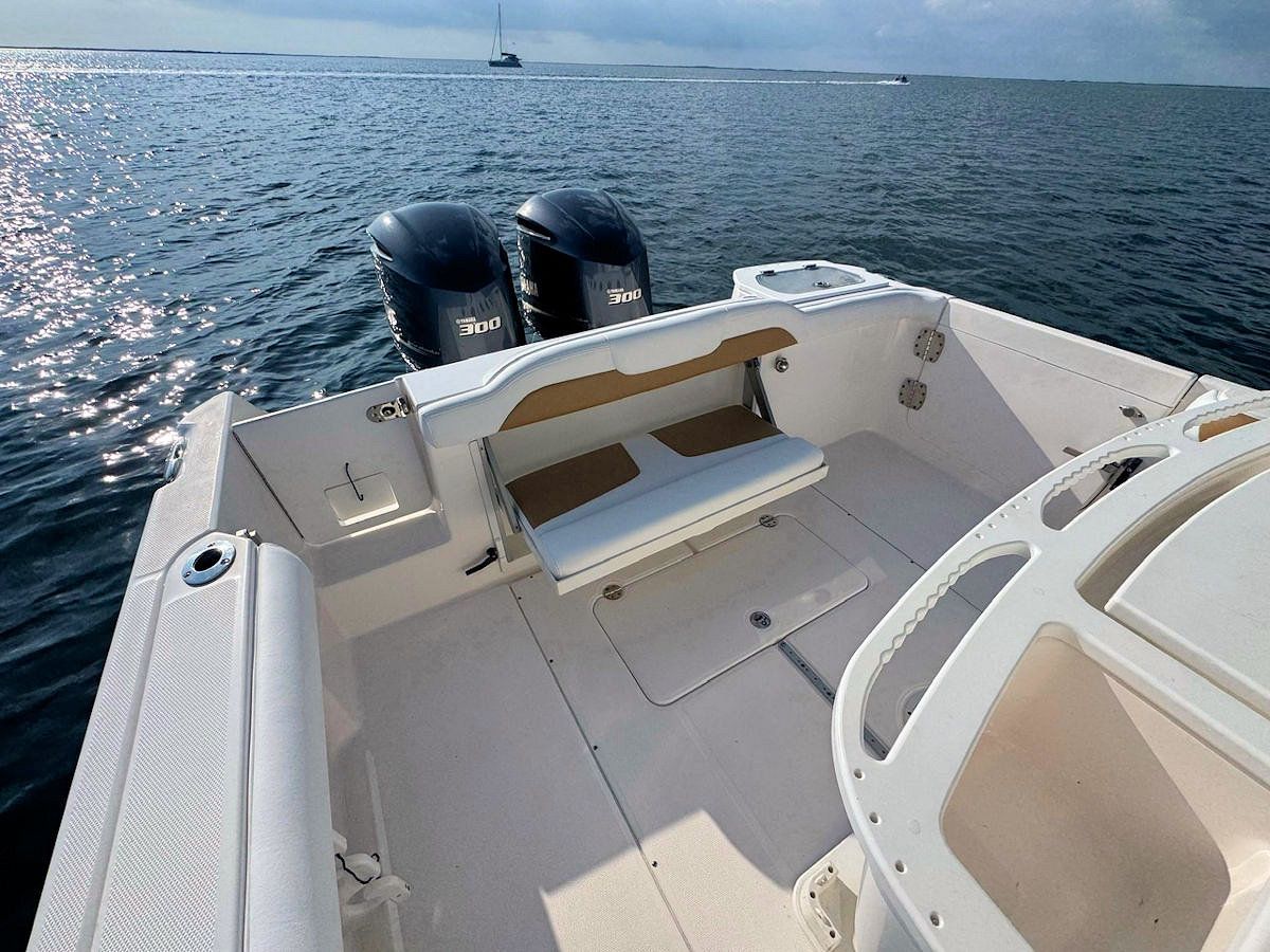 Back deck of a white motorboat with dual black outboard motors. Ocean background.