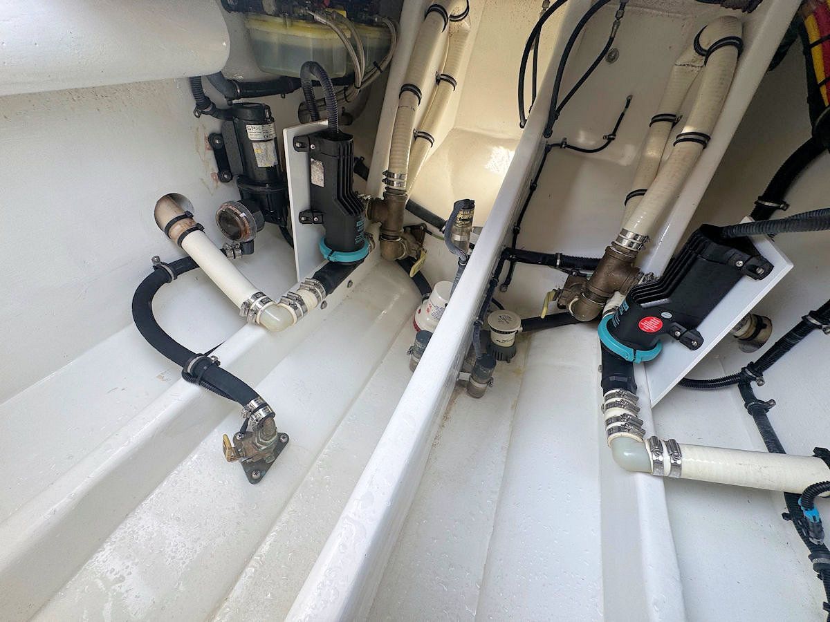 Boat plumbing system with white pipes, black hoses, and various valves in a confined space.